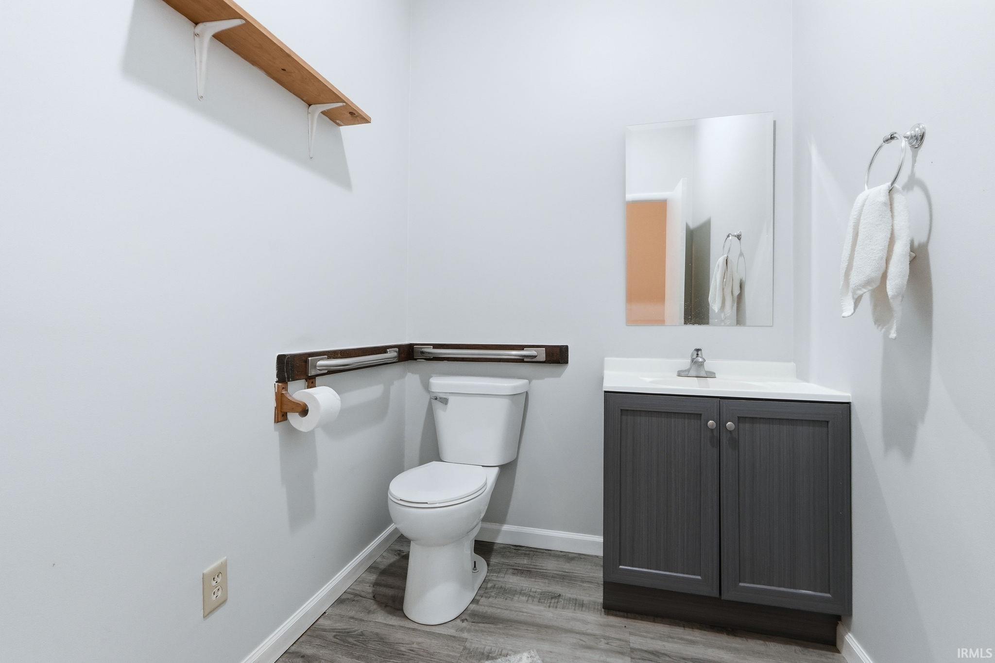 Powder room featuring a white toilet, gray vanity with white countertop, chrome faucet, wall-mounted mirror, and wood-finish flooring