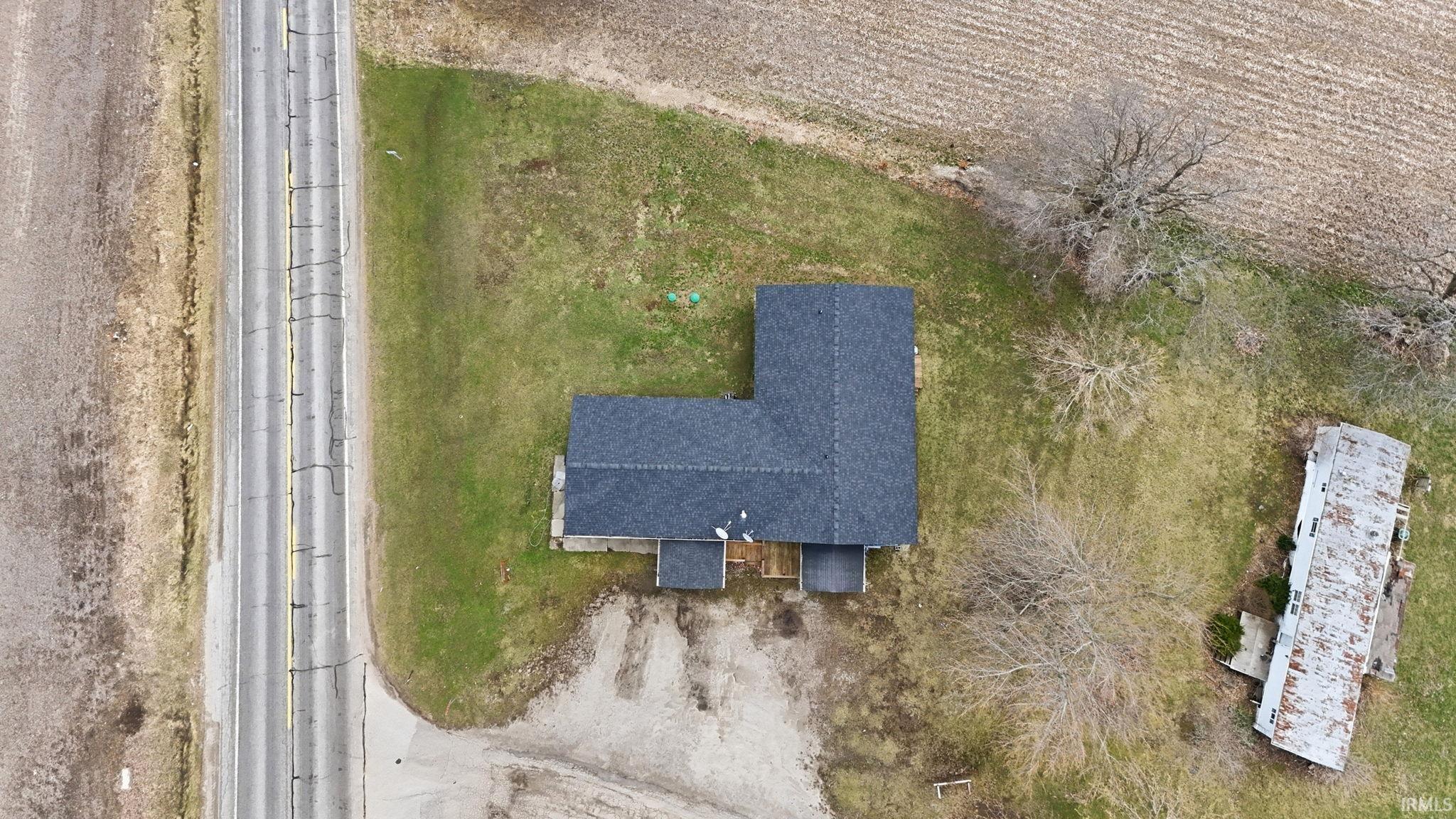 Aerial perspective showcasing a property with a dark shingle roof, surrounded by expansive green space