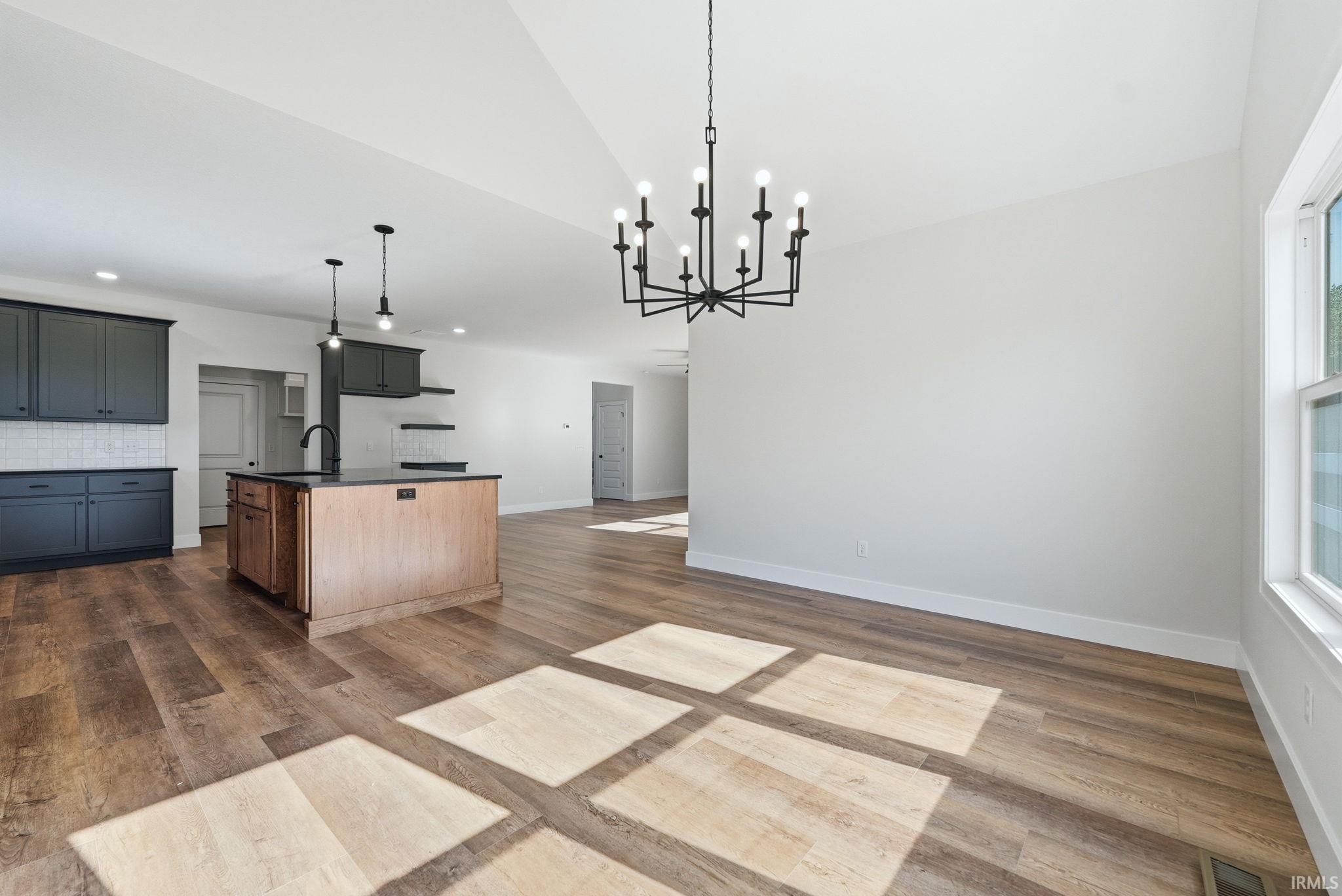 Open-concept living space featuring wood-finish flooring, a kitchen island with dark countertops, dark cabinetry, and a black chandelier