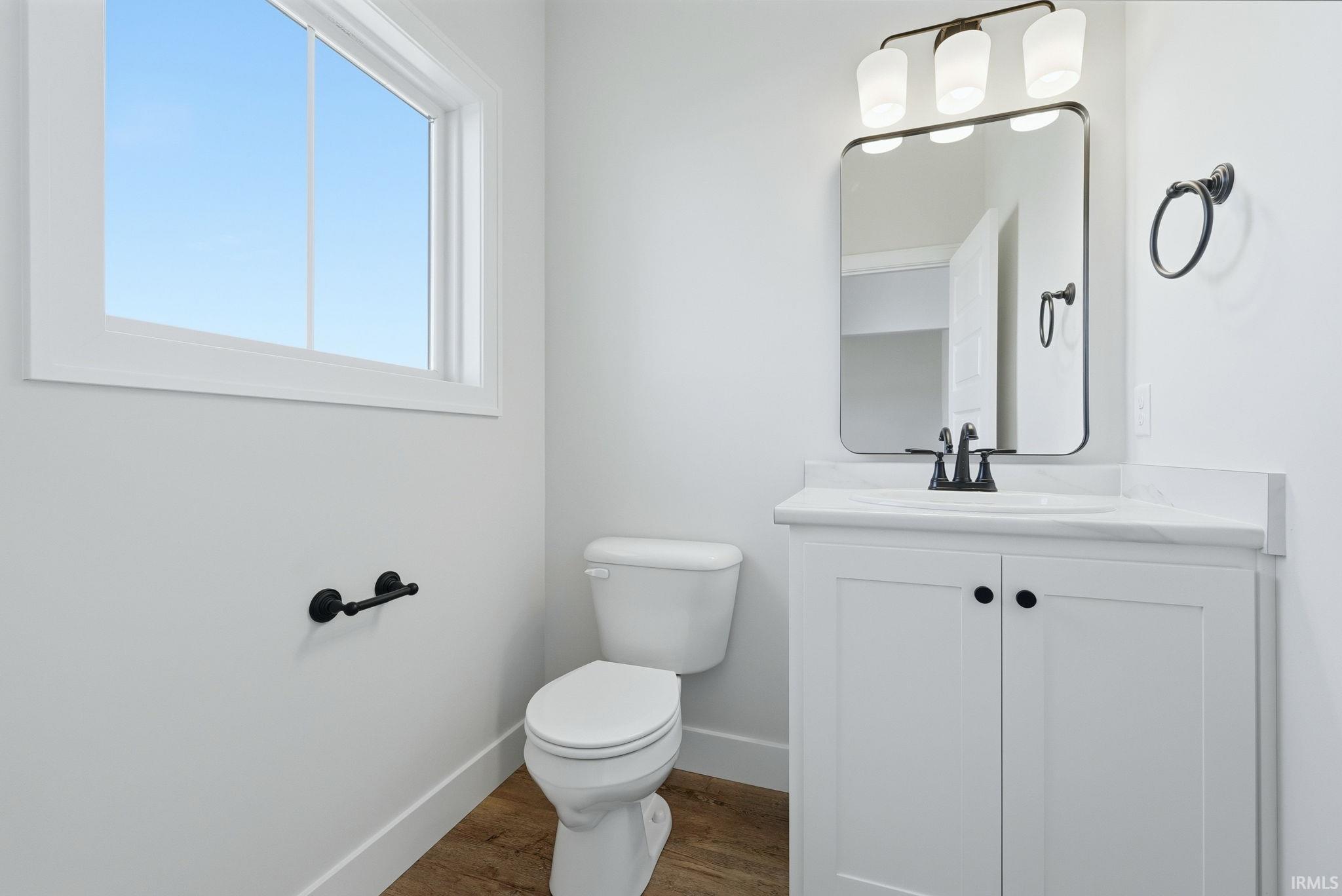 Bathroom featuring a white vanity with a rectangular sink, a framed mirror, a three-light vanity fixture, and wood-finish flooring