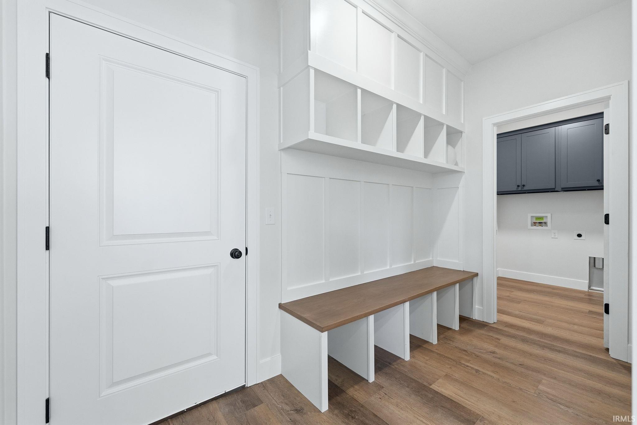 Entryway mudroom featuring built-in storage cubbies, a wood-finish bench, white paneled wainscoting, and wood-finish flooring