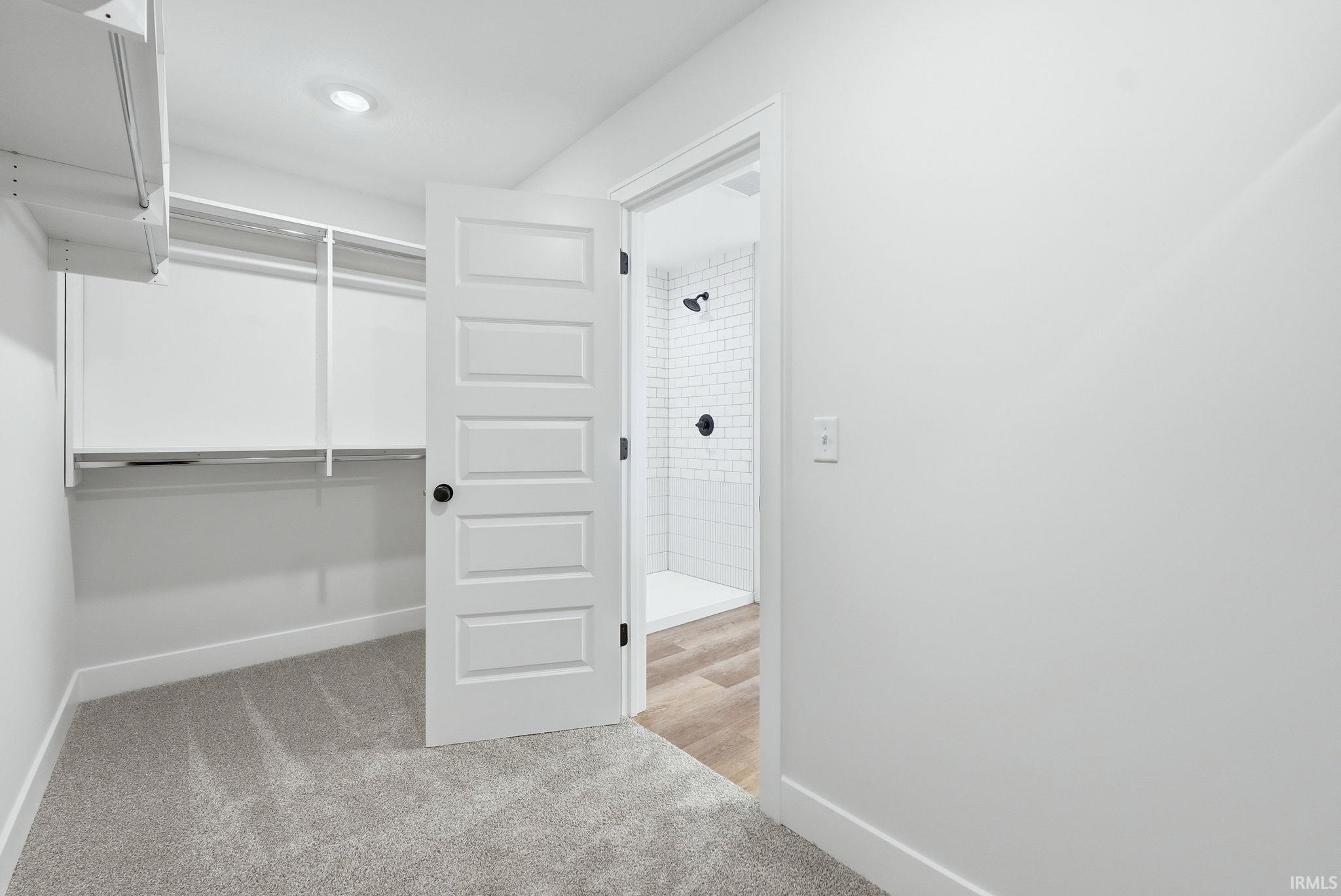 Walk-in closet featuring light gray carpeting, recessed lighting, and white shelving with hanging rods