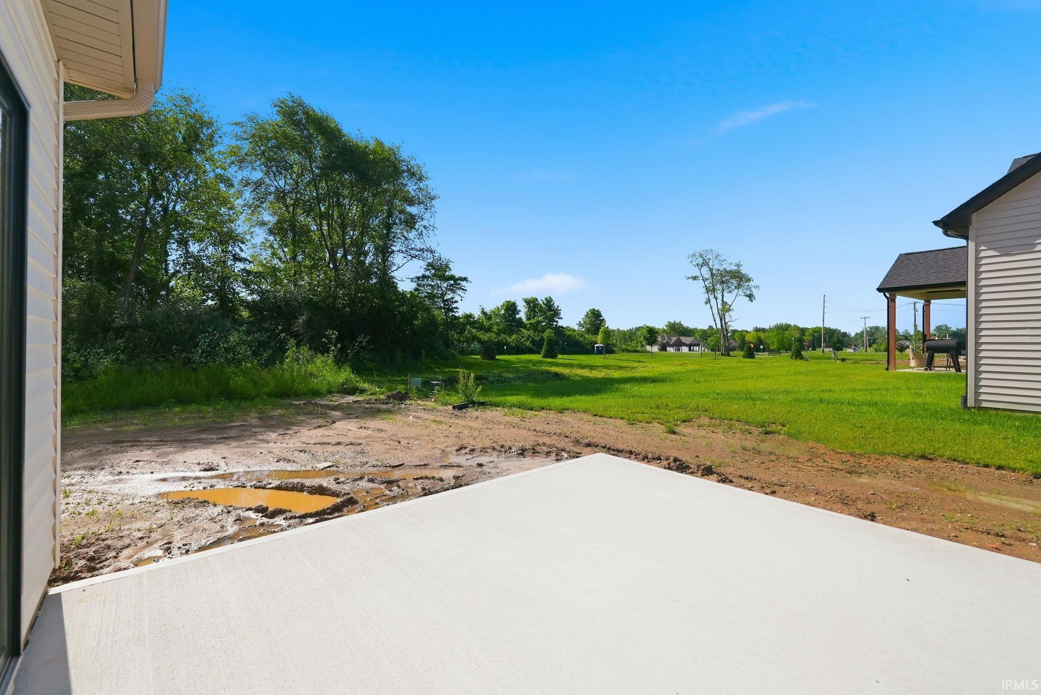 Expansive backyard featuring a new concrete patio, green lawn, and mature perimeter trees
