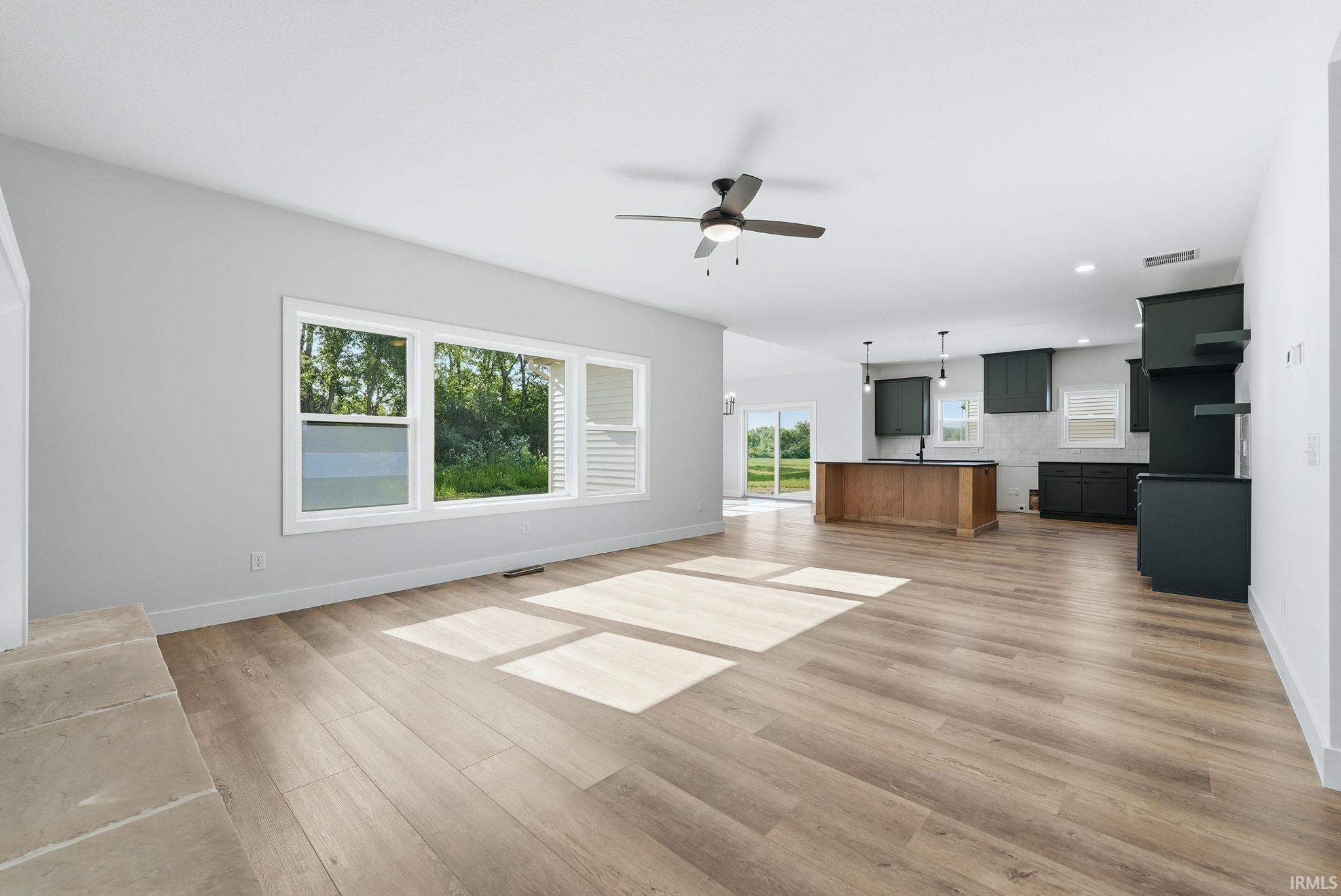 Open-concept living space featuring wood-finish flooring, a contemporary ceiling fan, and a wide window arrangement