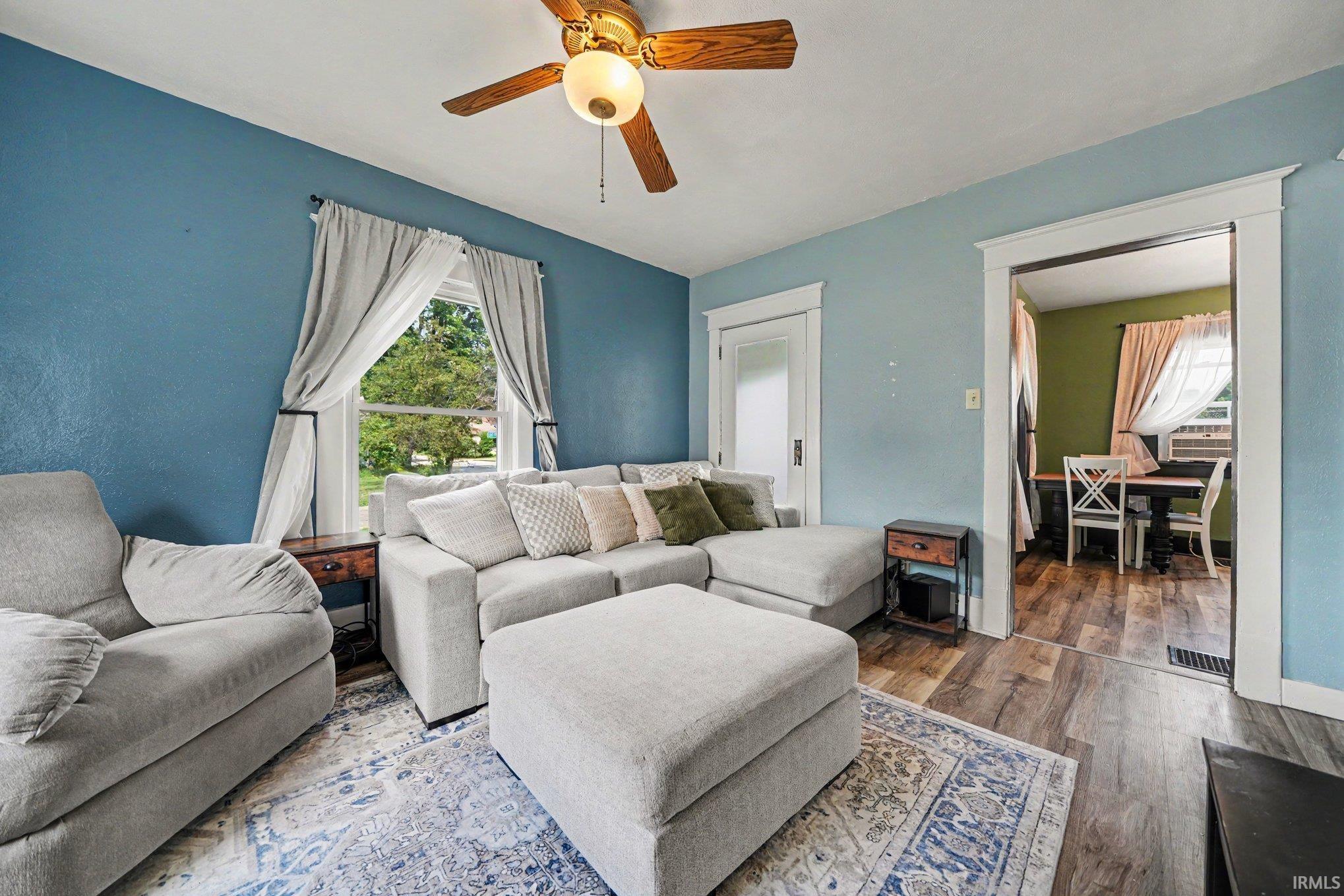 Living area featuring wood-finish flooring and a wood-bladed ceiling fan with integrated lighting