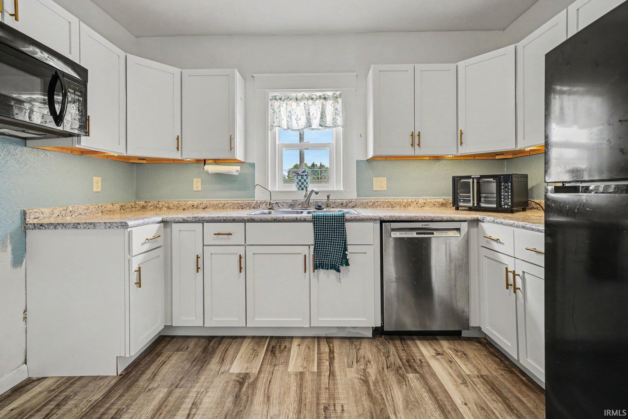 U-shaped kitchen featuring white cabinetry with gold-toned hardware, wood-finish flooring, a stainless steel dishwasher, and a built-in microwave