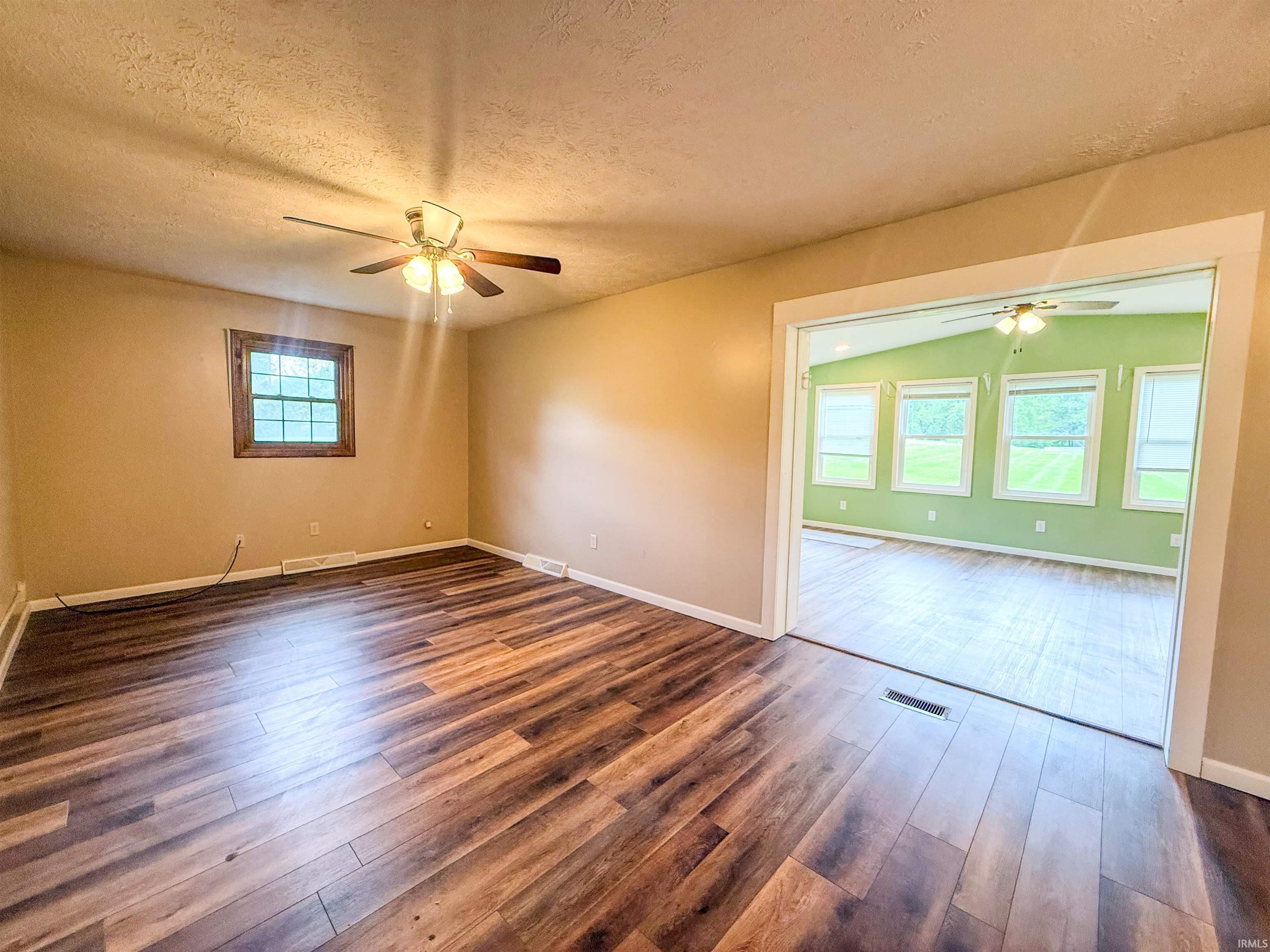 Spacious interior featuring wood-finish flooring, a ceiling fan with integrated lighting, and a large window providing ambient light