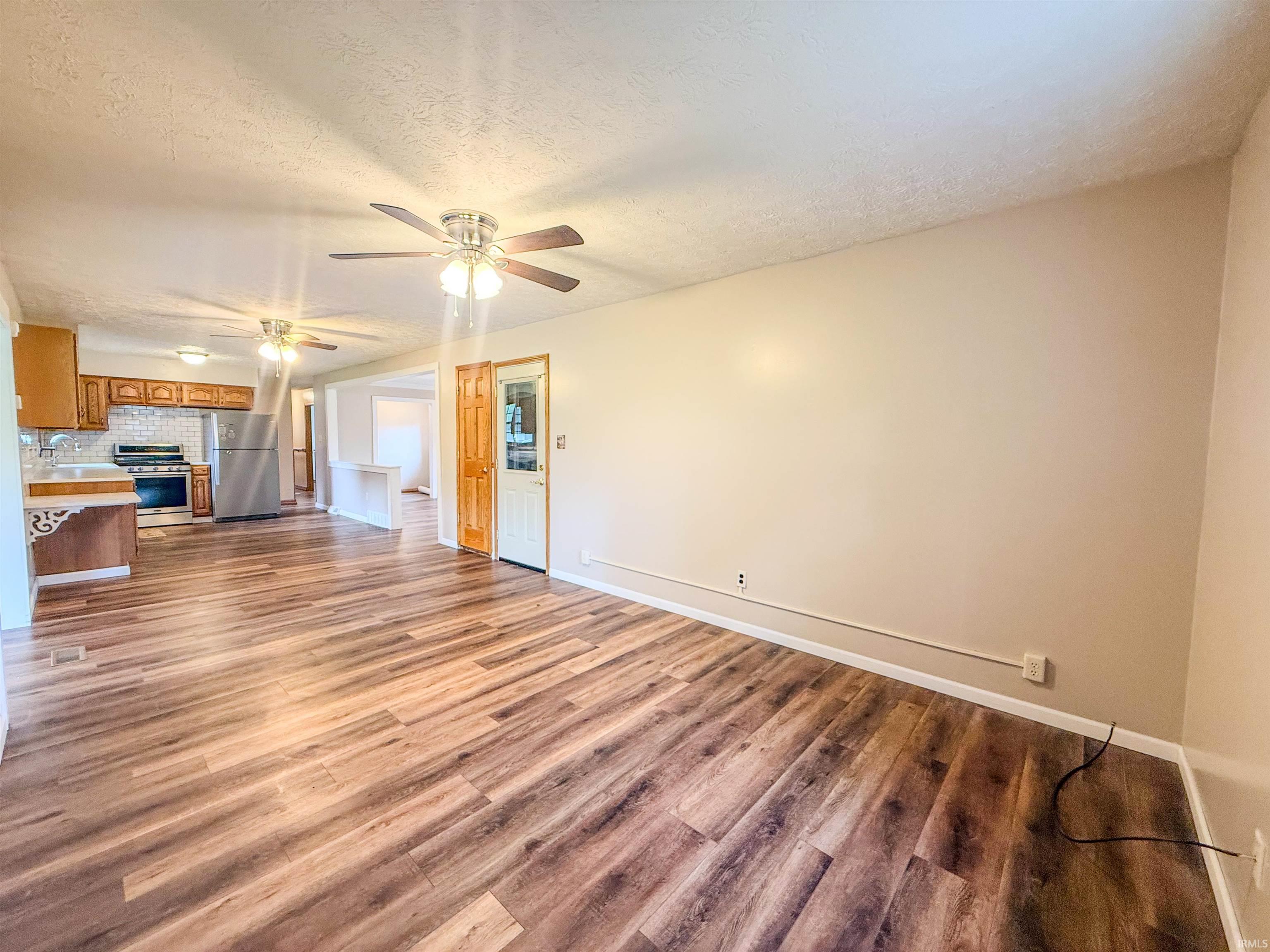 Spacious open-concept living area featuring wood-finish flooring, neutral wall tones, and multiple ceiling fans