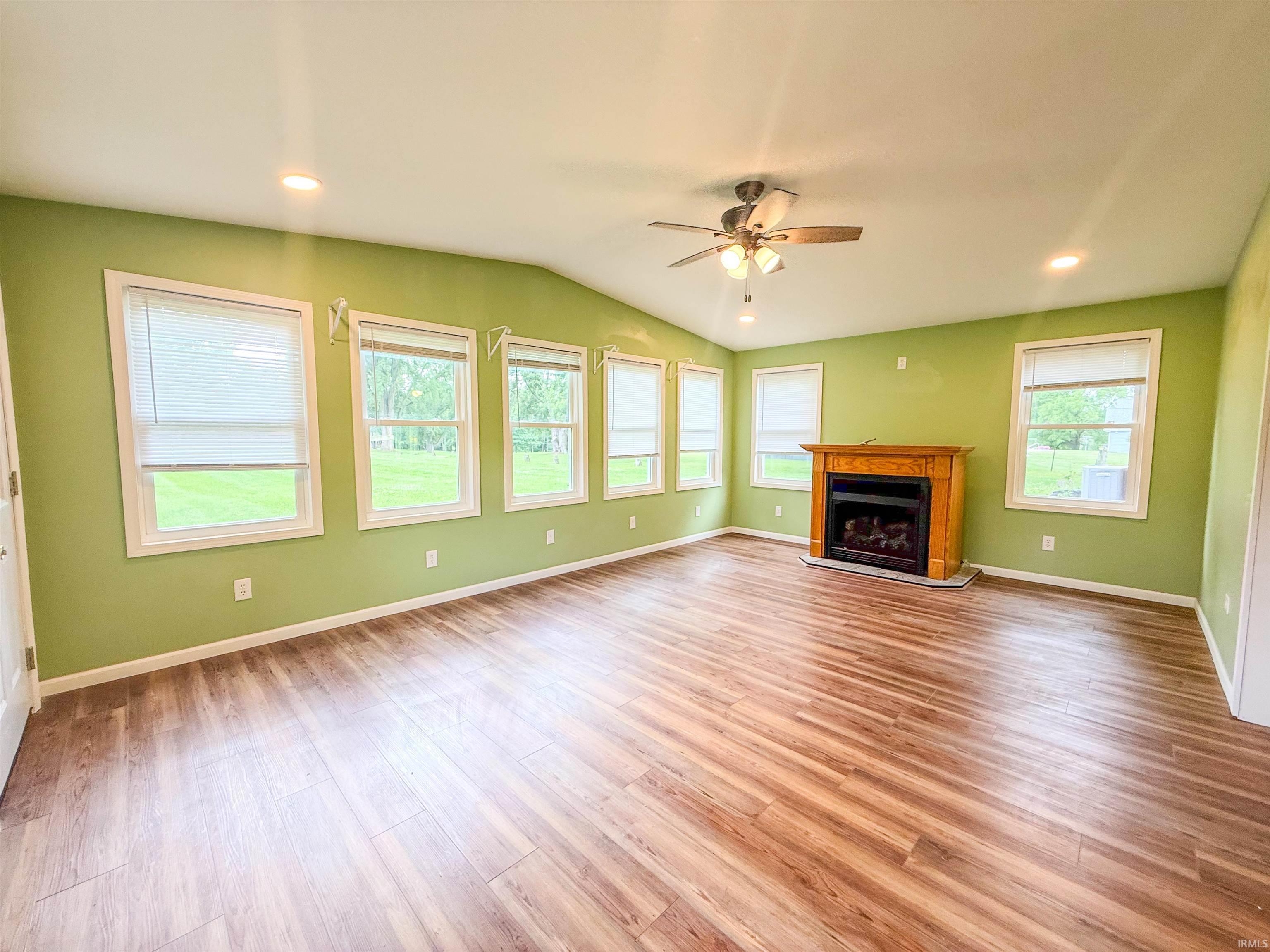 Spacious room featuring wood-finish flooring, a vaulted ceiling, and multiple windows