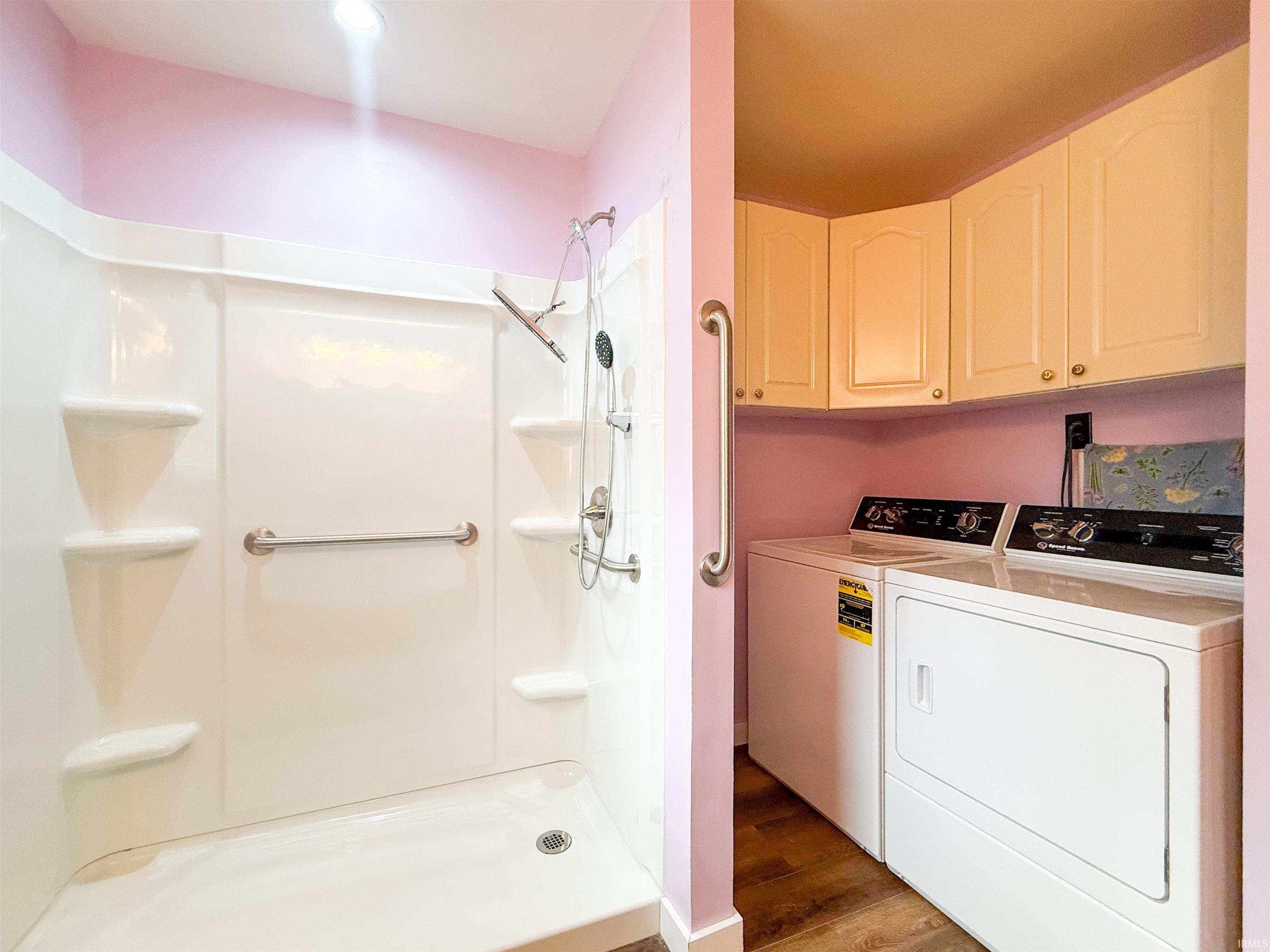 Integrated utility space featuring a white shower stall with built-in shelving and grab bars, alongside a dedicated laundry area with stacked appliances and cream-colored upper cabinetry