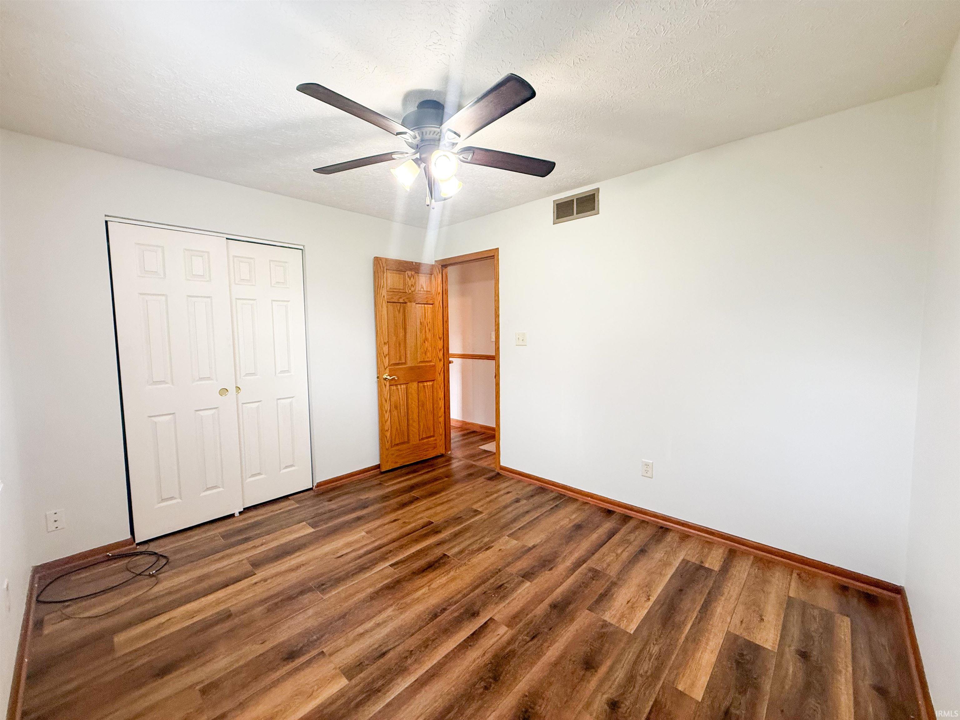 Interior room featuring wood-finish flooring, a ceiling fan with integrated lighting, a bi-fold closet with white panel doors, and a wood-paneled door