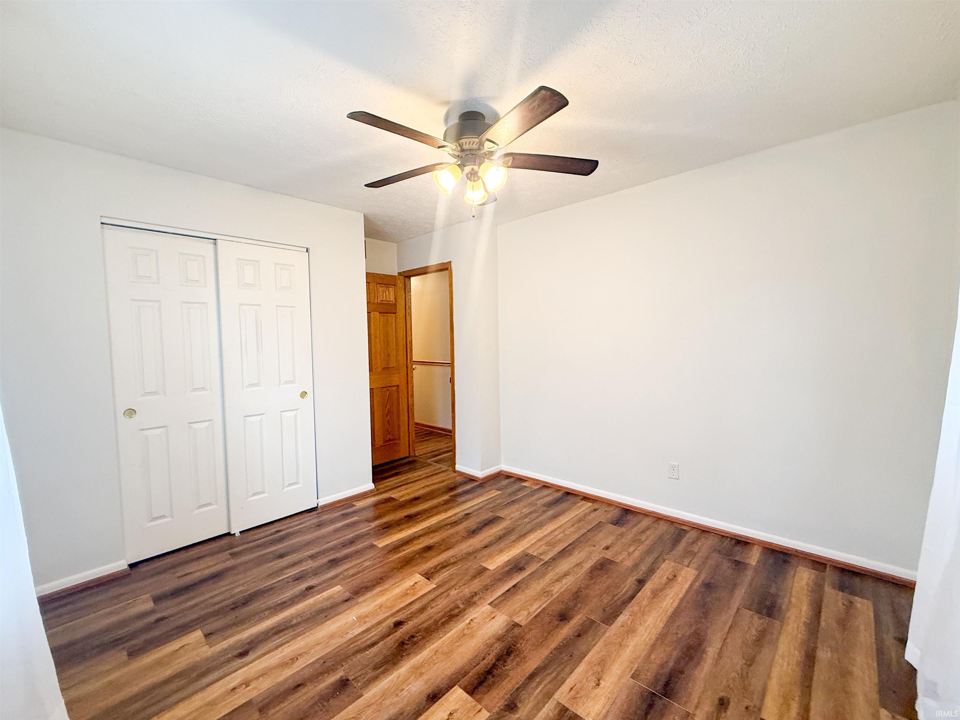 Room featuring wood-finish flooring, a ceiling fan with light fixture, and white painted walls