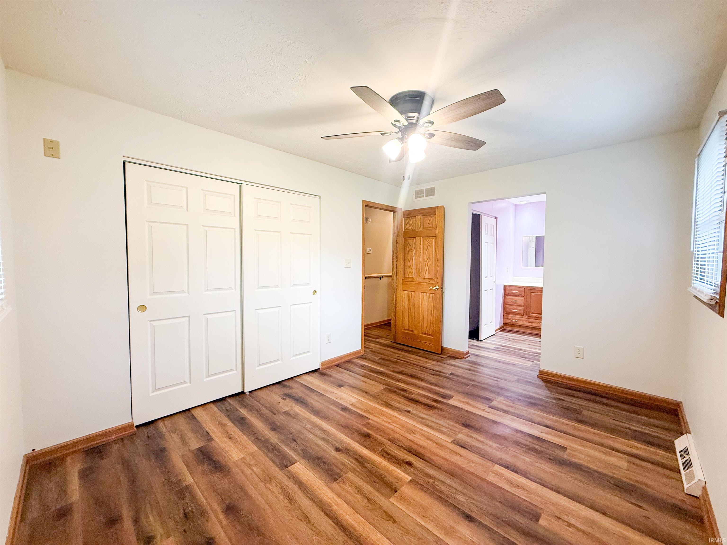 Room featuring wood-finish flooring, white walls, and a ceiling fan