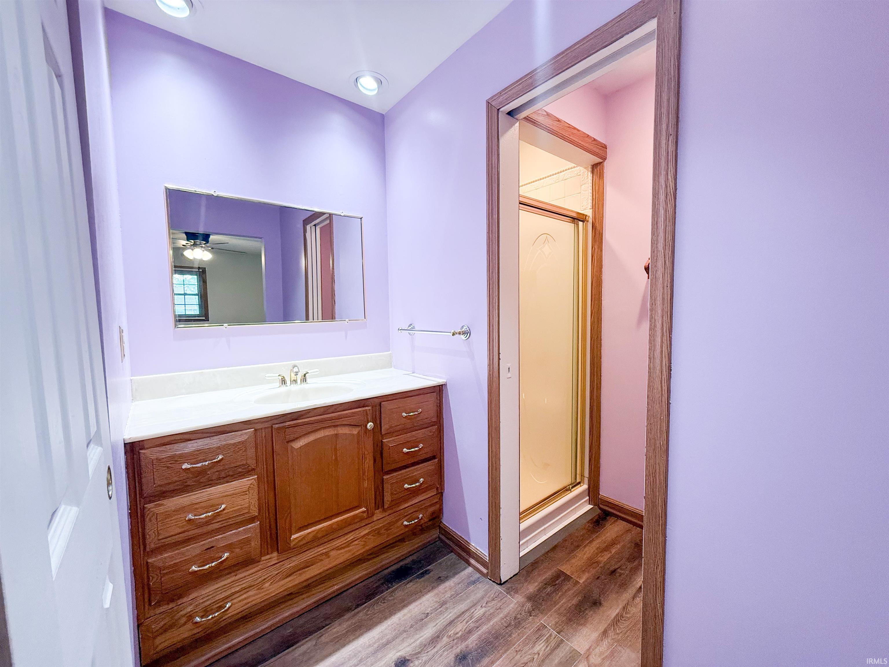 Bathroom featuring a wood-finish vanity with an integrated sink and light-toned countertop, recessed ceiling lighting, and wood-finish flooring