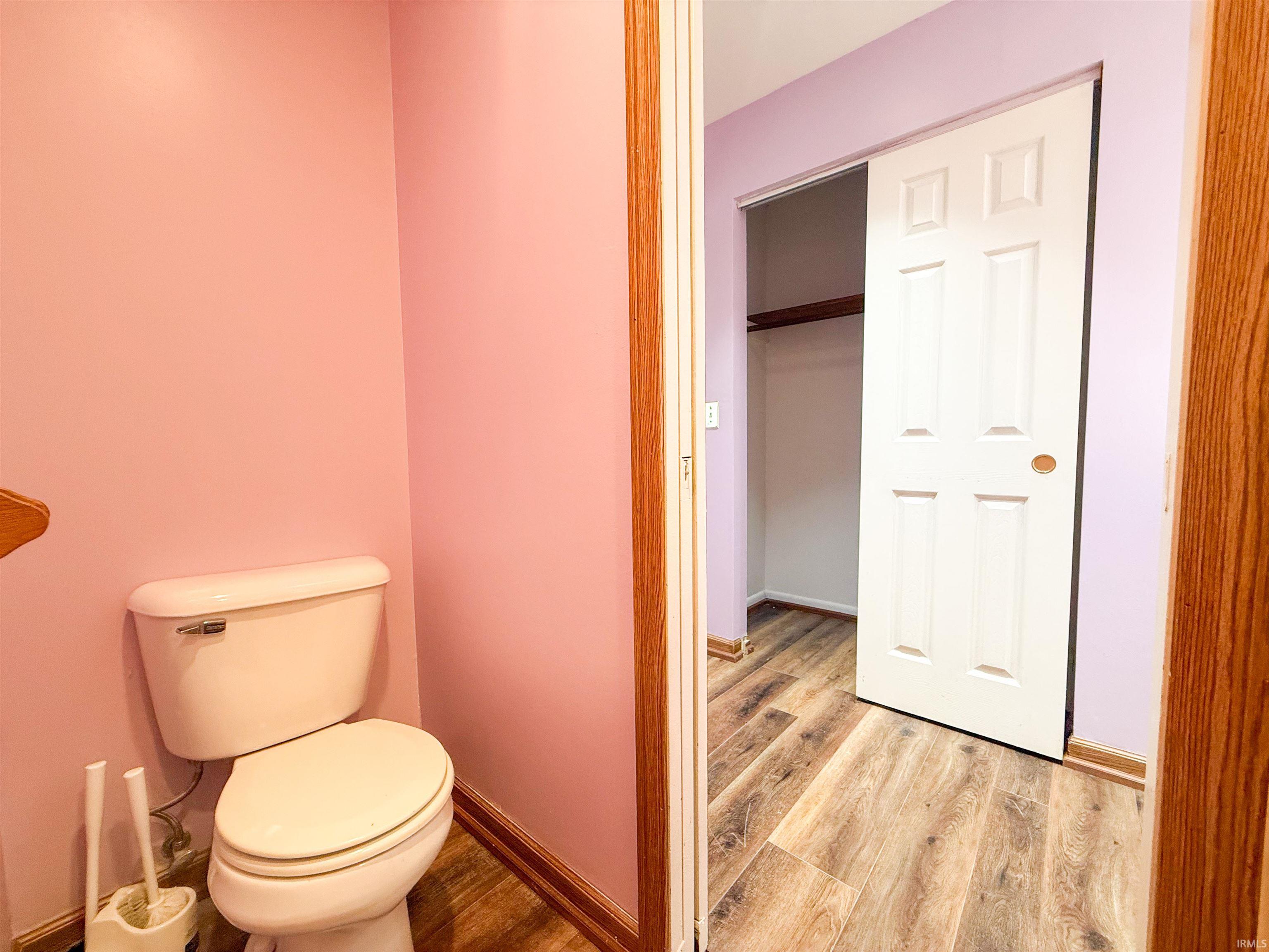 Bathroom featuring a white toilet, wood-finish flooring, and a sliding closet door