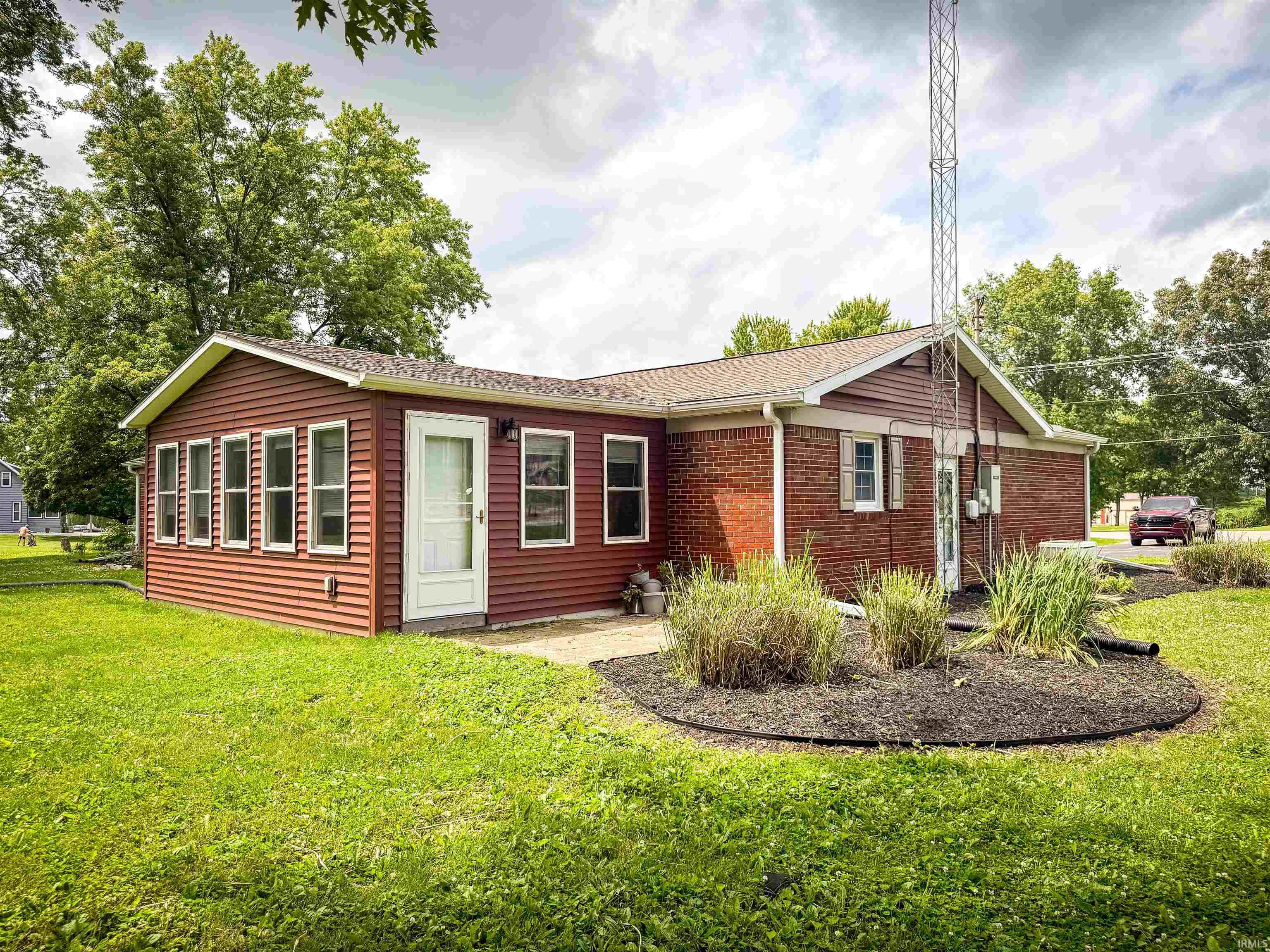Exterior featuring a brick facade, red siding, multiple windows, a white entry door, and a landscaped garden bed