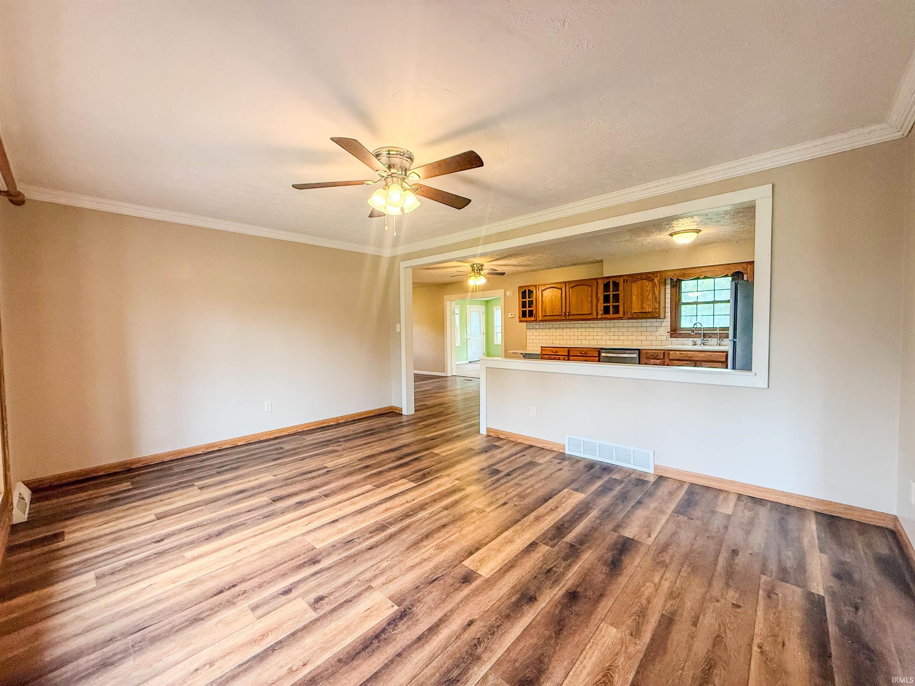 Open-concept living space featuring wood-finish flooring, a ceiling fan, and a pass-through window to the kitchen