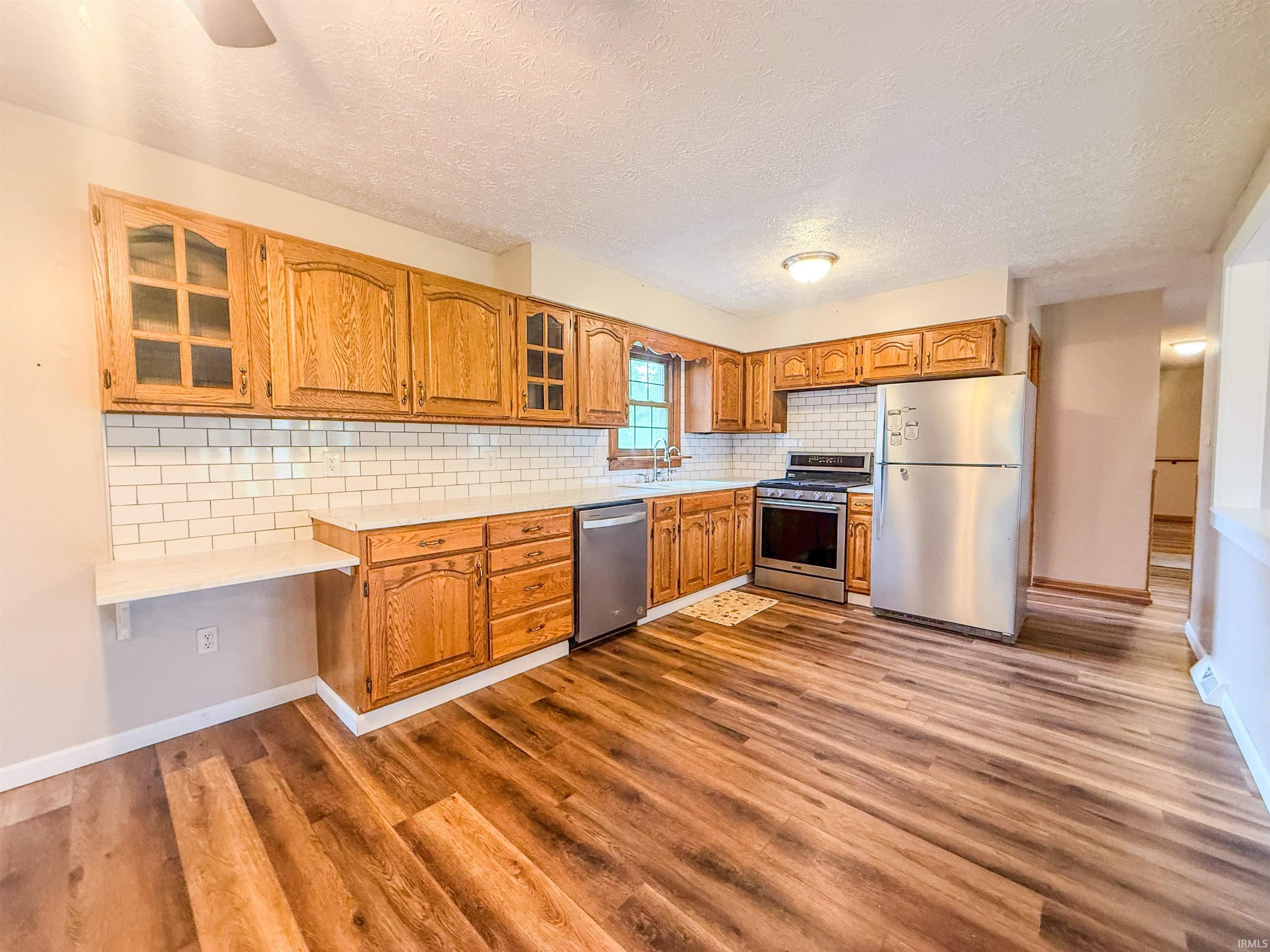 Kitchen featuring wood-finish flooring, wood cabinetry, white subway tile backsplash, white countertops, and stainless steel appliances