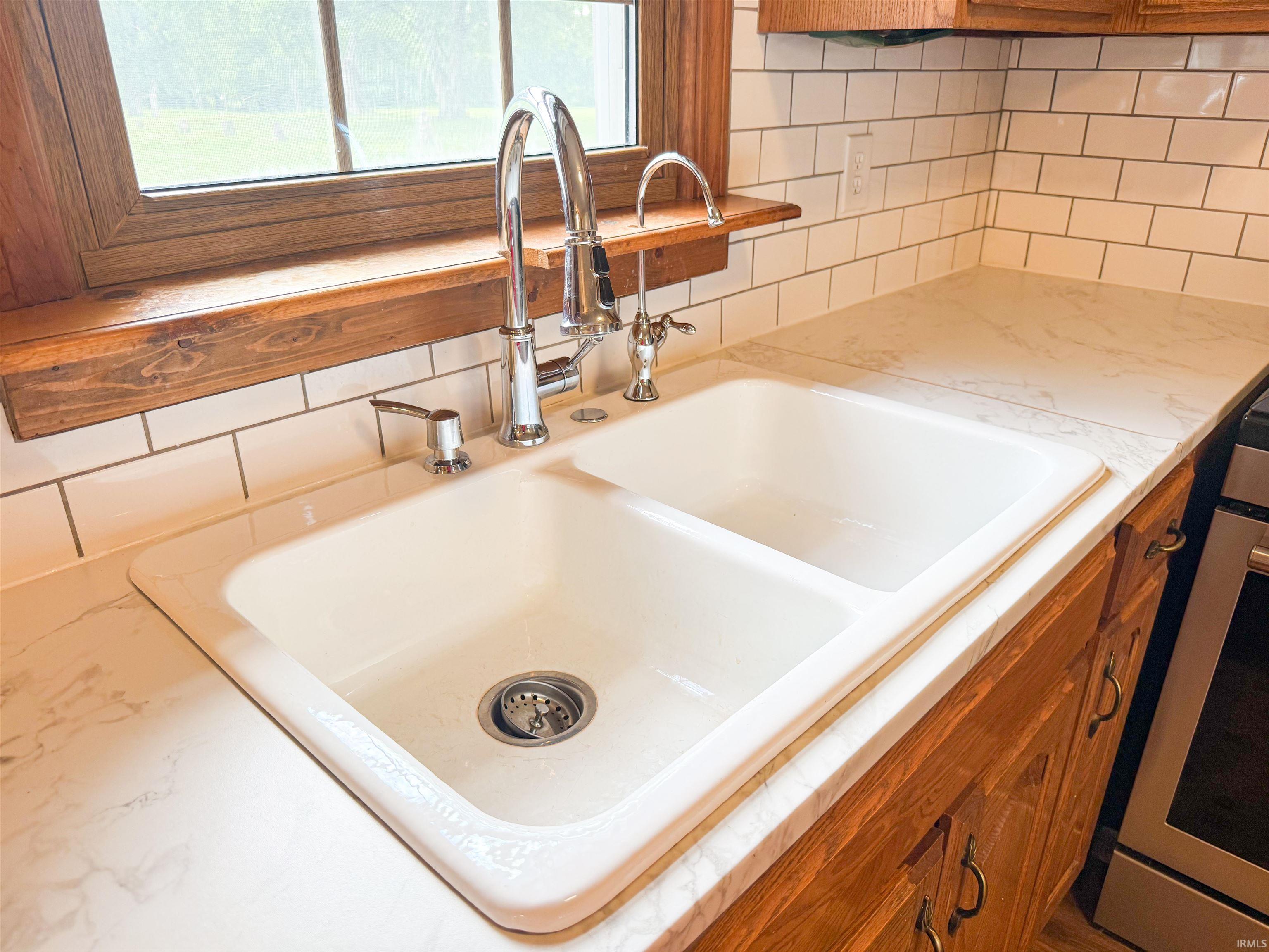 Dual-basin kitchen sink with chrome fixtures, set in a light-toned countertop with a subway tile backsplash