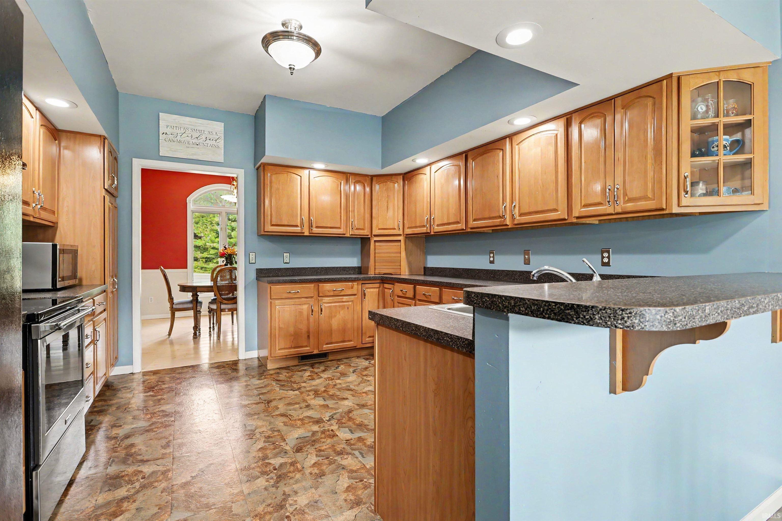 Expansive kitchen featuring wood cabinetry, stone-look countertops, and a built-in breakfast bar