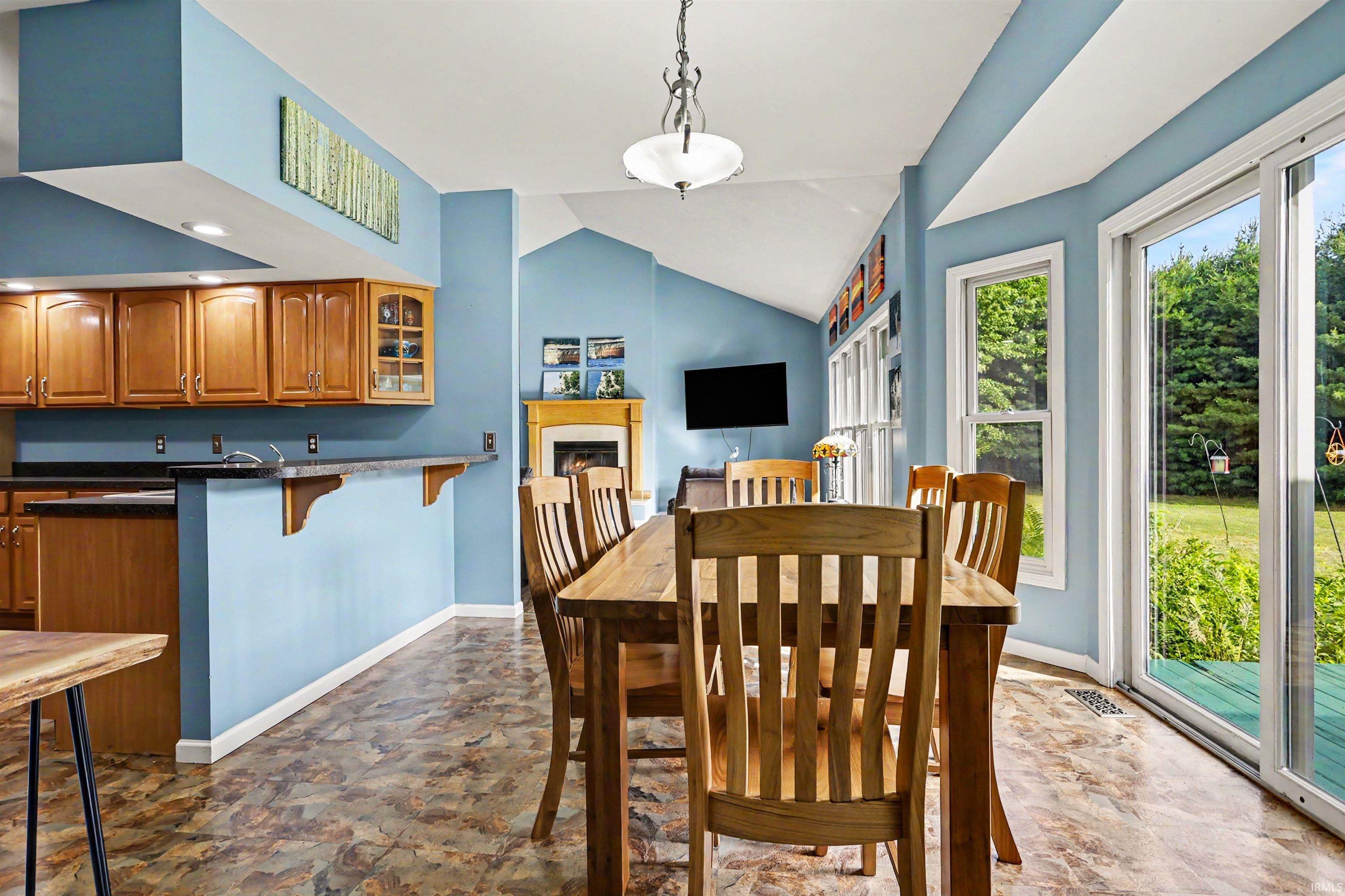 Open-concept dining area featuring wood-finish flooring, a vaulted ceiling, and a prominent fireplace with a mantel