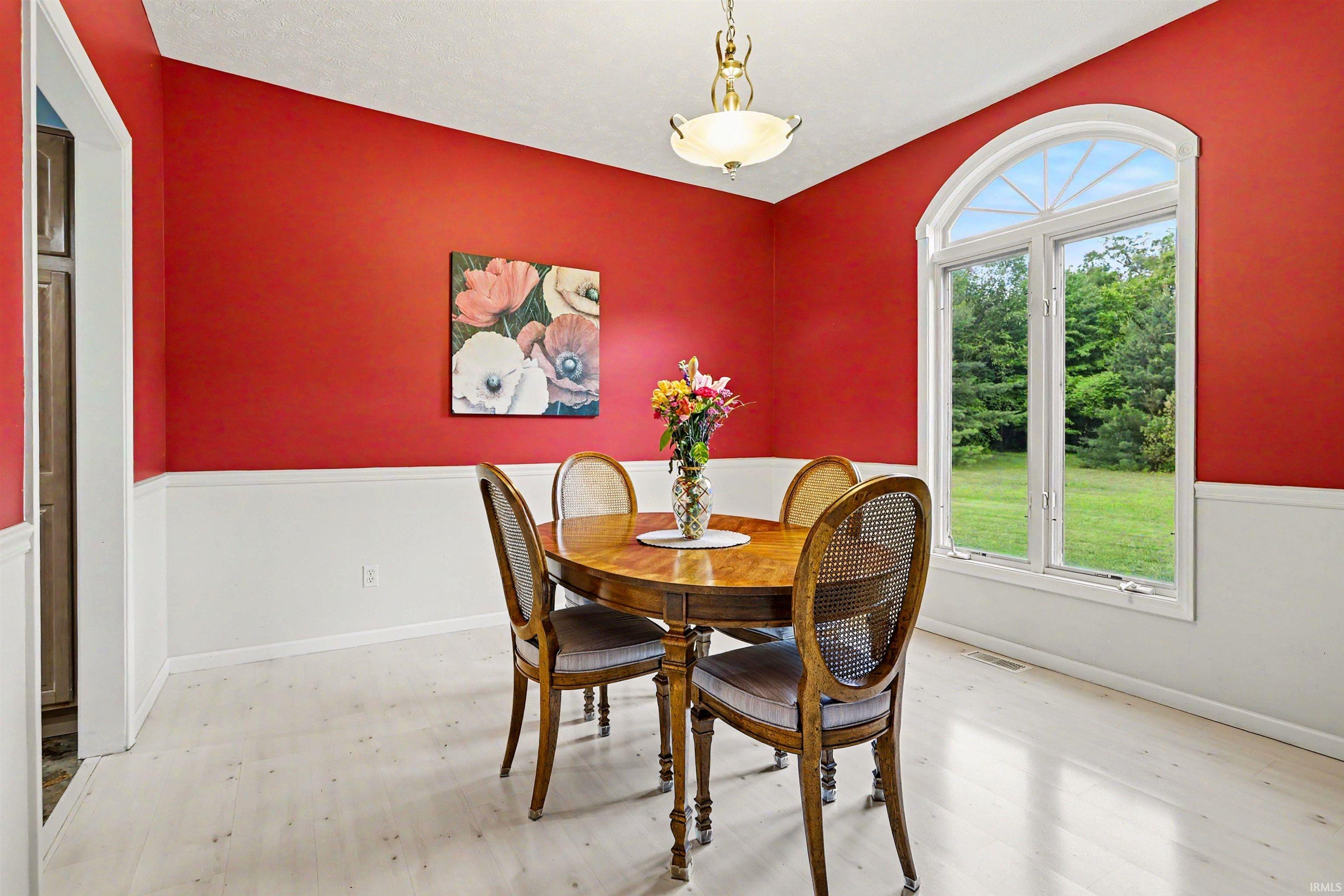 Dining area featuring a prominent arched window, two-tone wall treatment, light wood-finish flooring, and an ornate ceiling light fixture