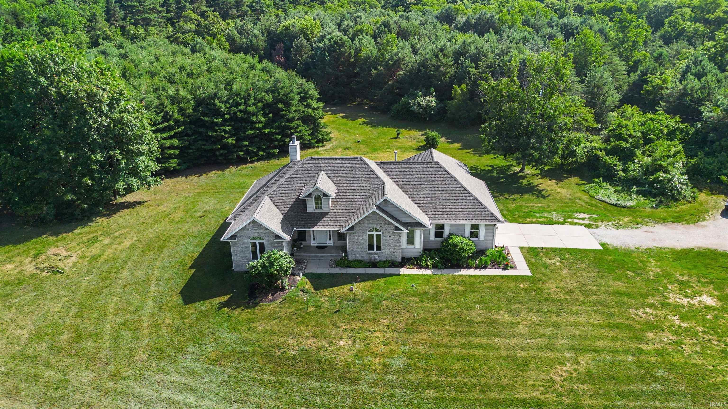 Expansive property featuring a single-story residence with a gray shingle roof, light-colored brick exterior, and dormer windows