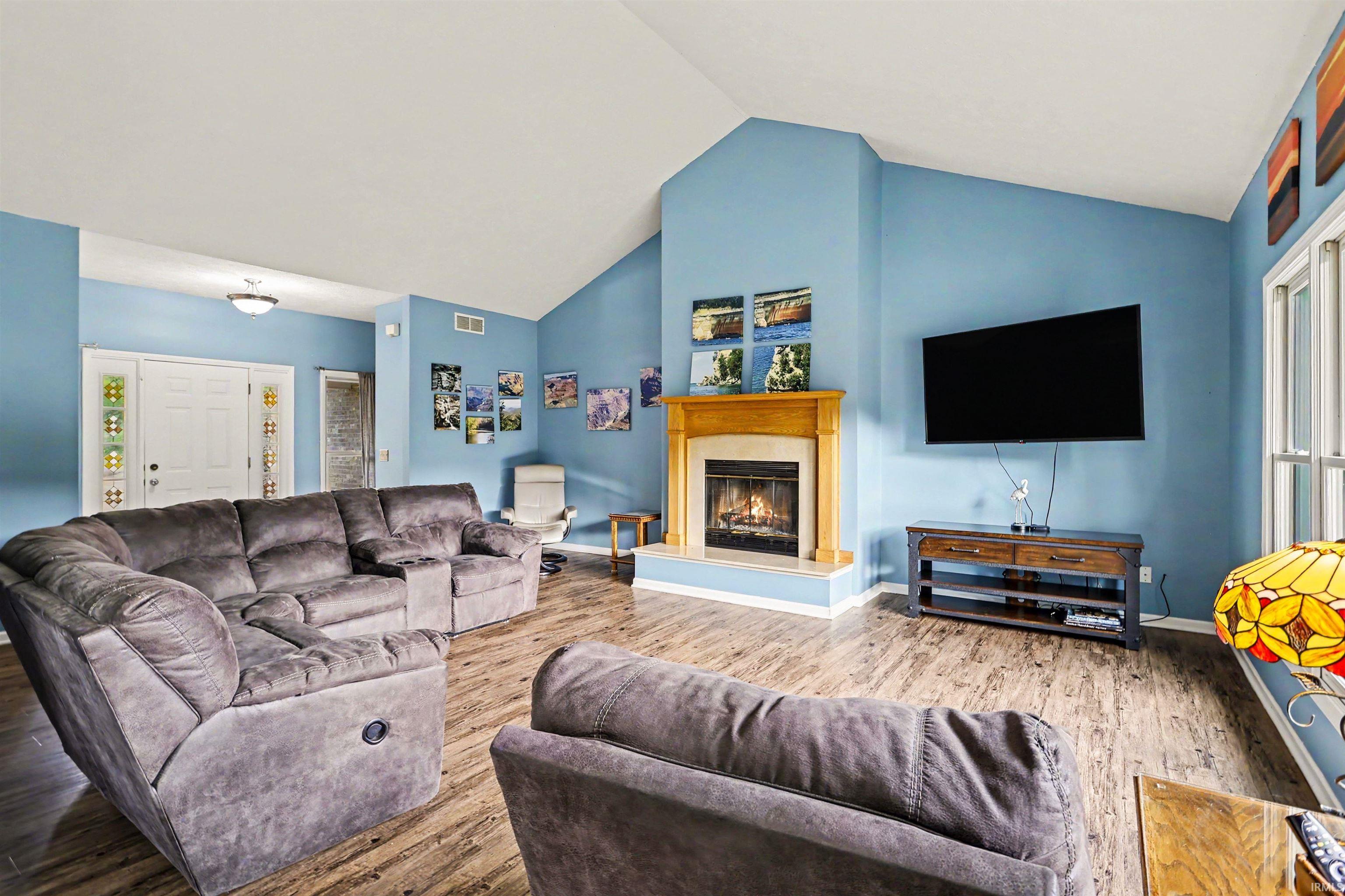 Vaulted living room featuring a fireplace with a wood mantle, wood-finish flooring, and a double-door entry