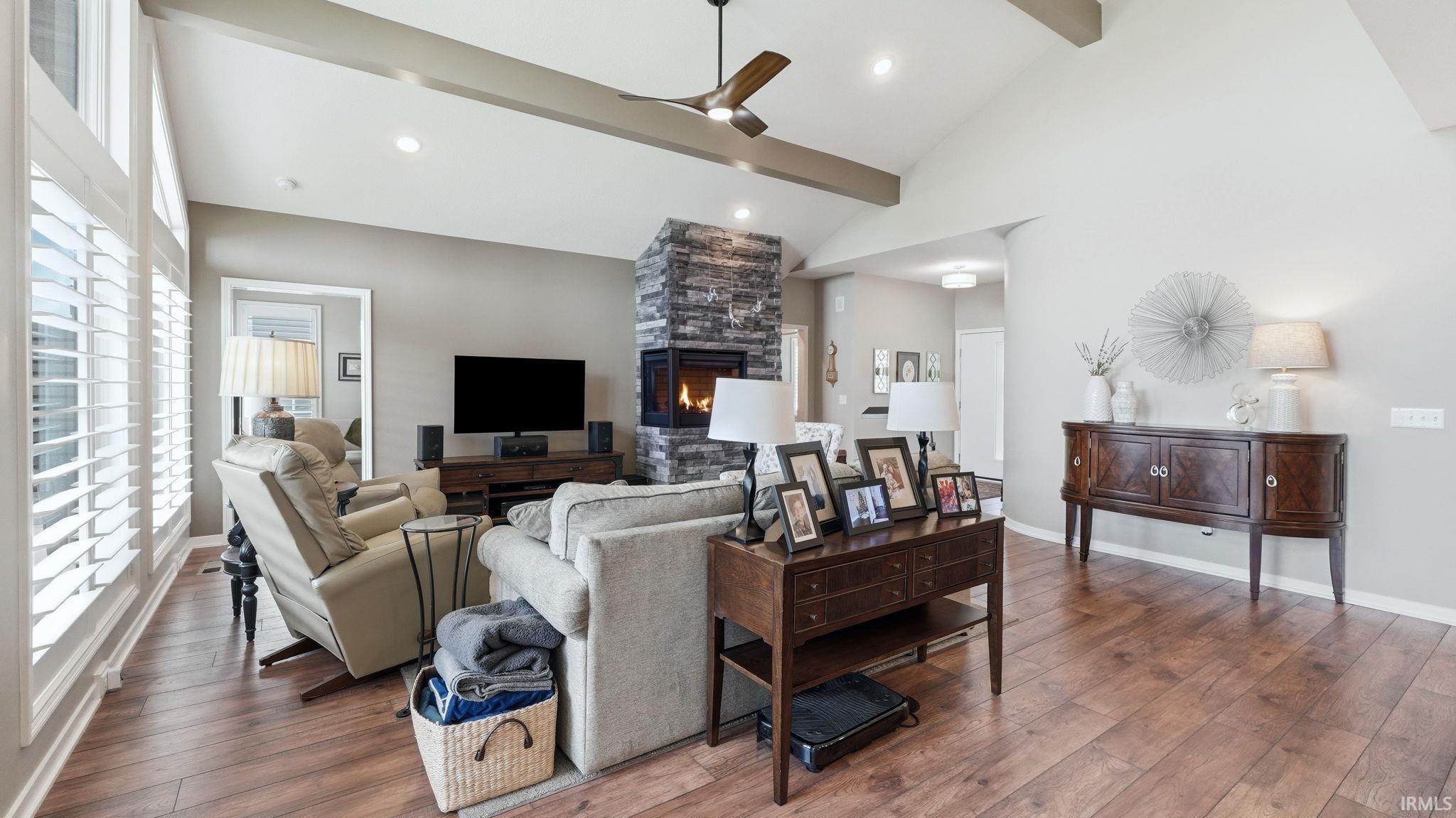 Spacious living area featuring wood-finish flooring, a vaulted ceiling with exposed beams, and a modern ceiling fan