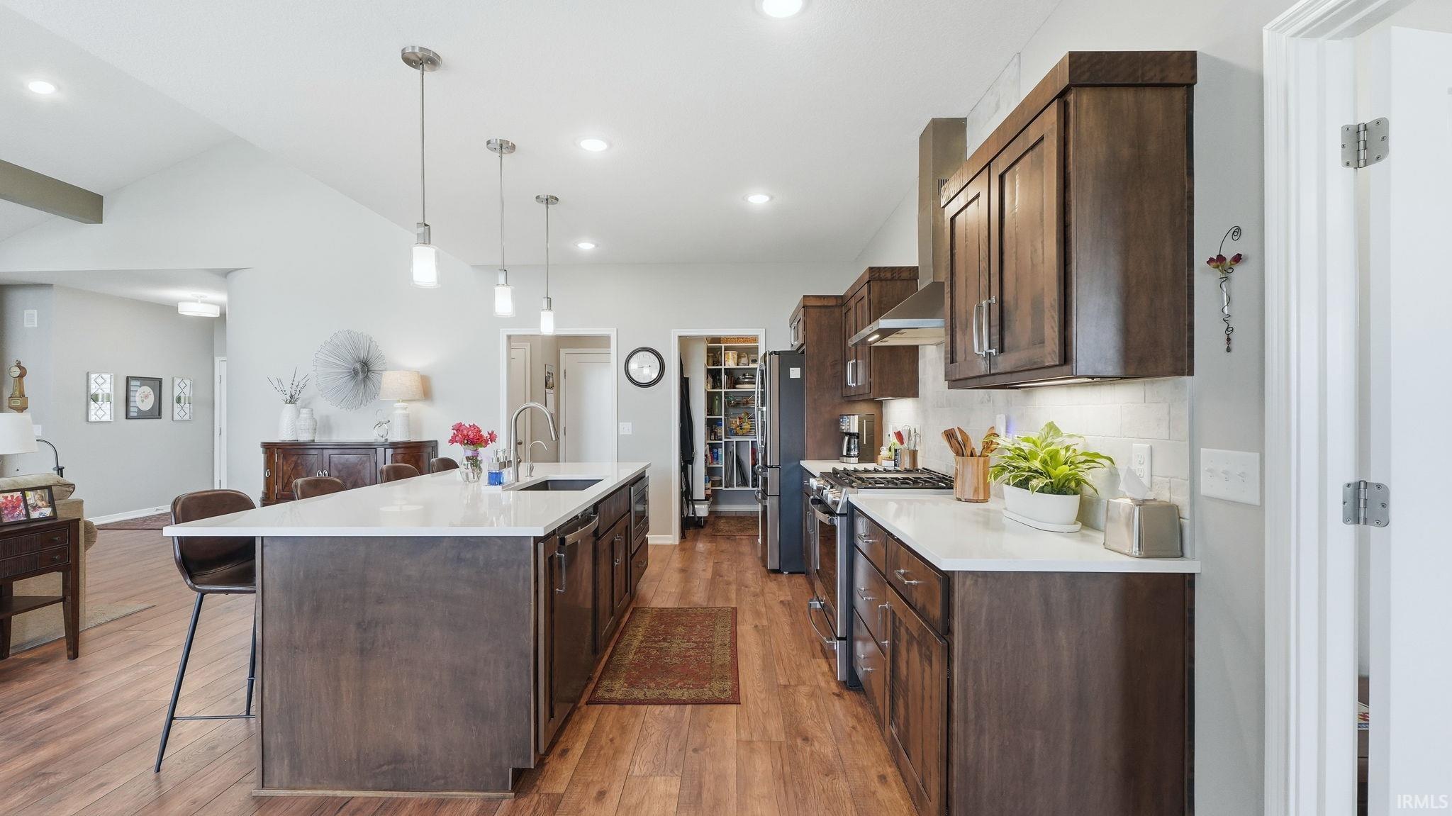 Open-concept kitchen featuring wood-finish flooring, dark wood cabinetry, white countertops, and a subway tile backsplash