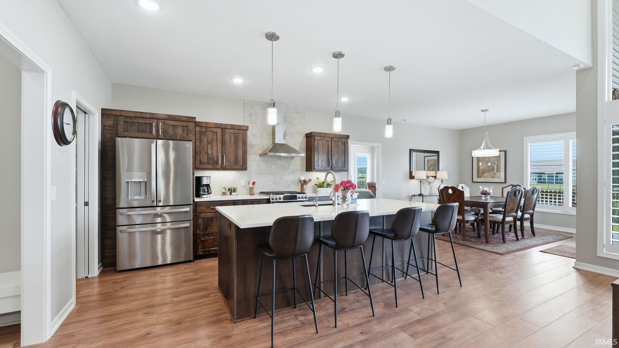 Spacious kitchen featuring an expansive central island with pendant lighting, stainless steel appliances, dark wood cabinetry, and wood-finish flooring