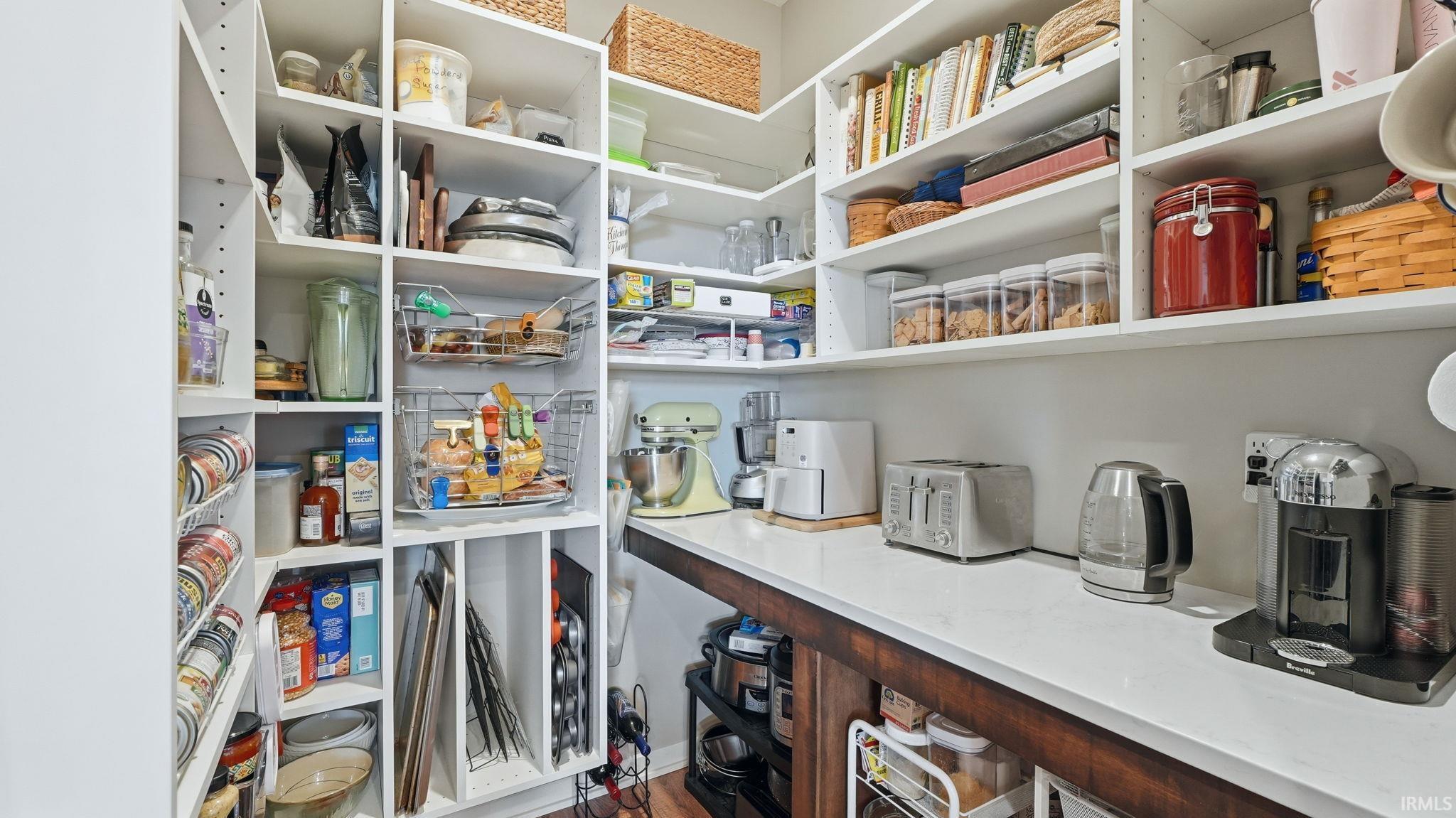 Walk-in pantry with extensive white built-in shelving, a wood-finish countertop, and integrated vertical storage compartments