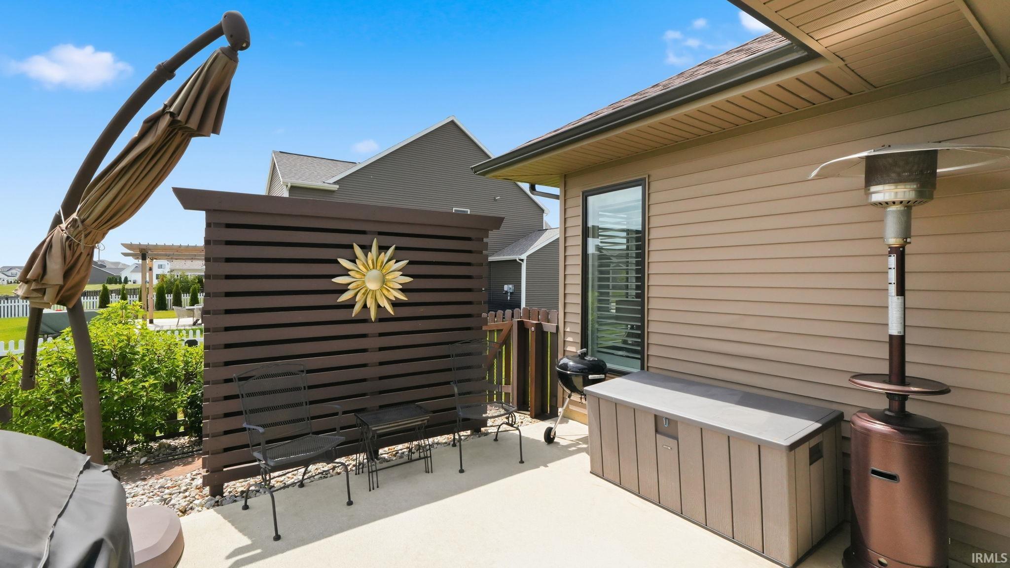 Spacious concrete patio featuring a slatted privacy screen, tan vinyl siding, a large exterior window, and a white picket fence
