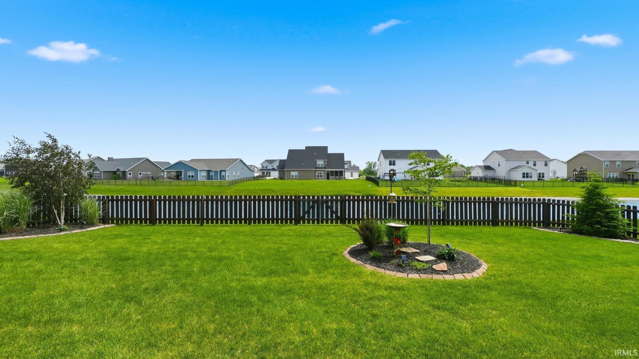 Expansive green lawn with a dark picket fence, a garden bed featuring decorative stone steps, and mature landscaping