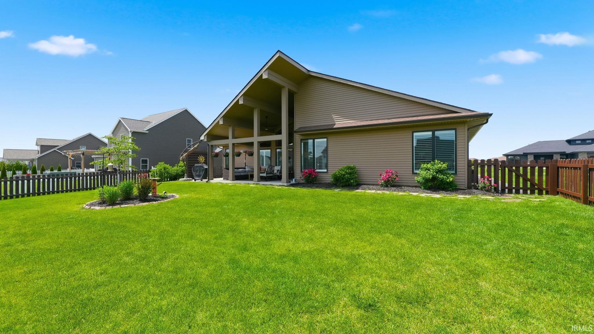 Expansive backyard featuring a large green lawn, brown siding, and a covered patio with high ceilings