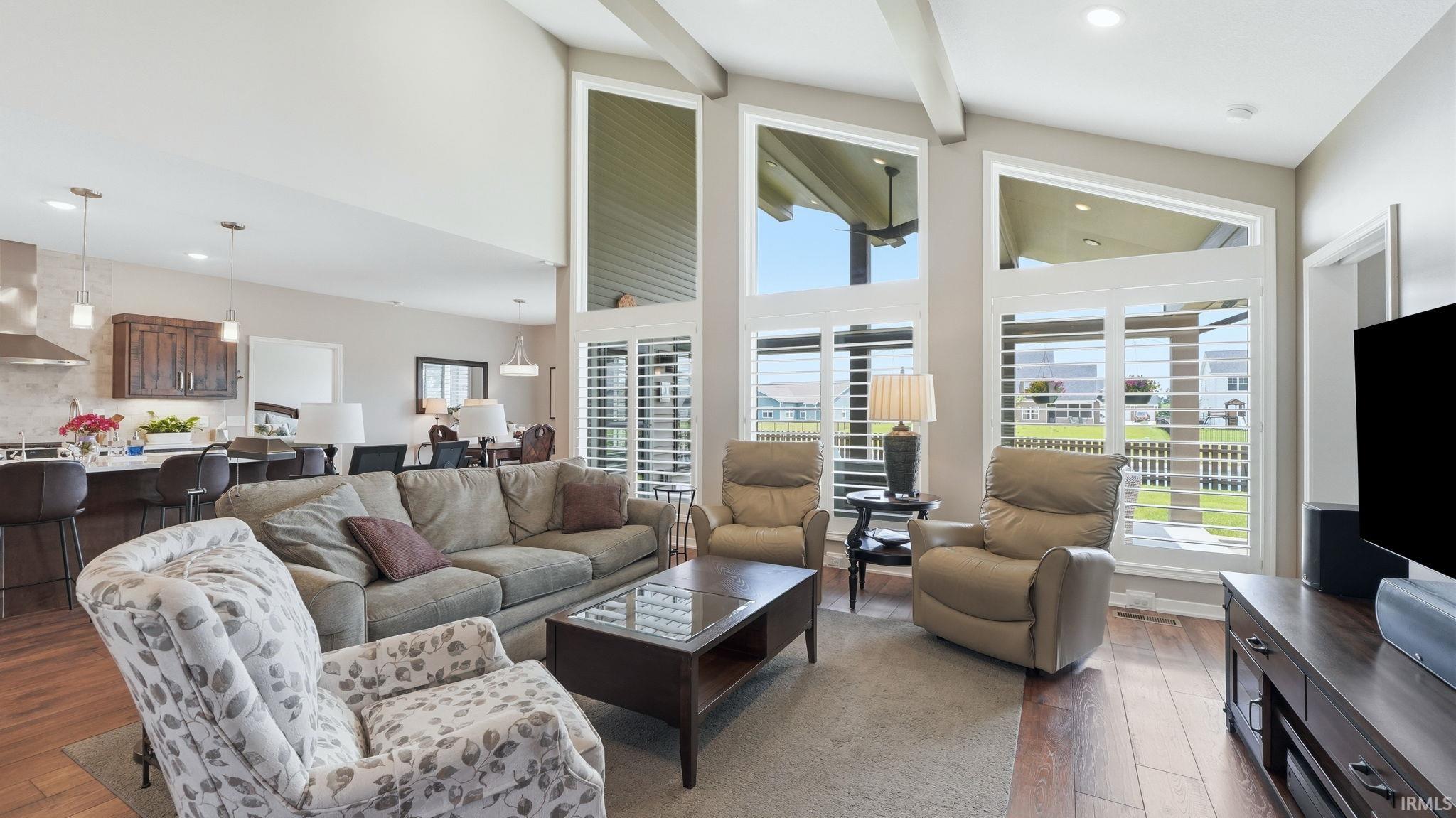Vaulted living room featuring wood-finish flooring, exposed ceiling beams, and a wall of windows with plantation shutters
