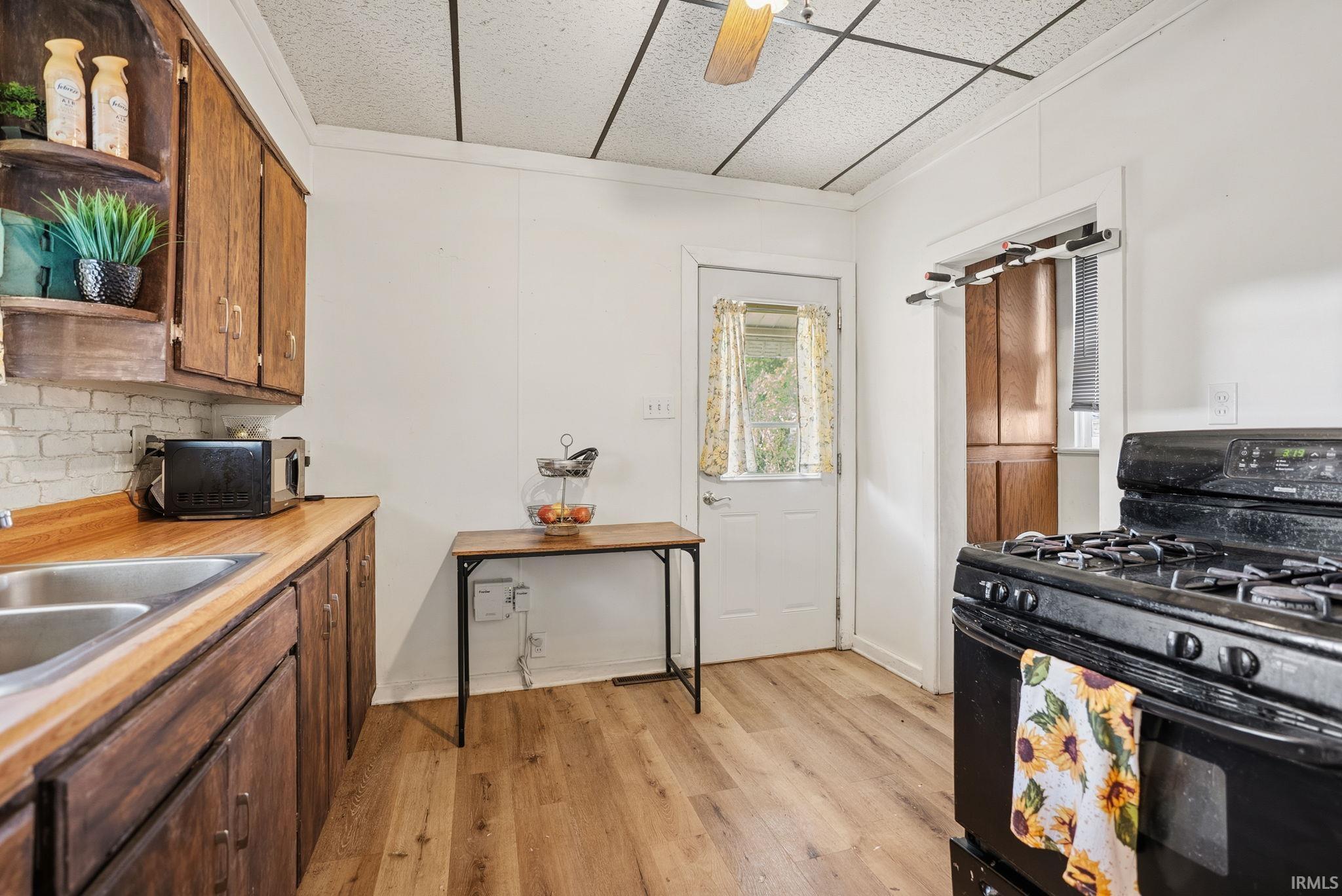 Kitchen featuring wood-finish flooring, wood cabinetry, a double basin stainless steel sink, and a black range