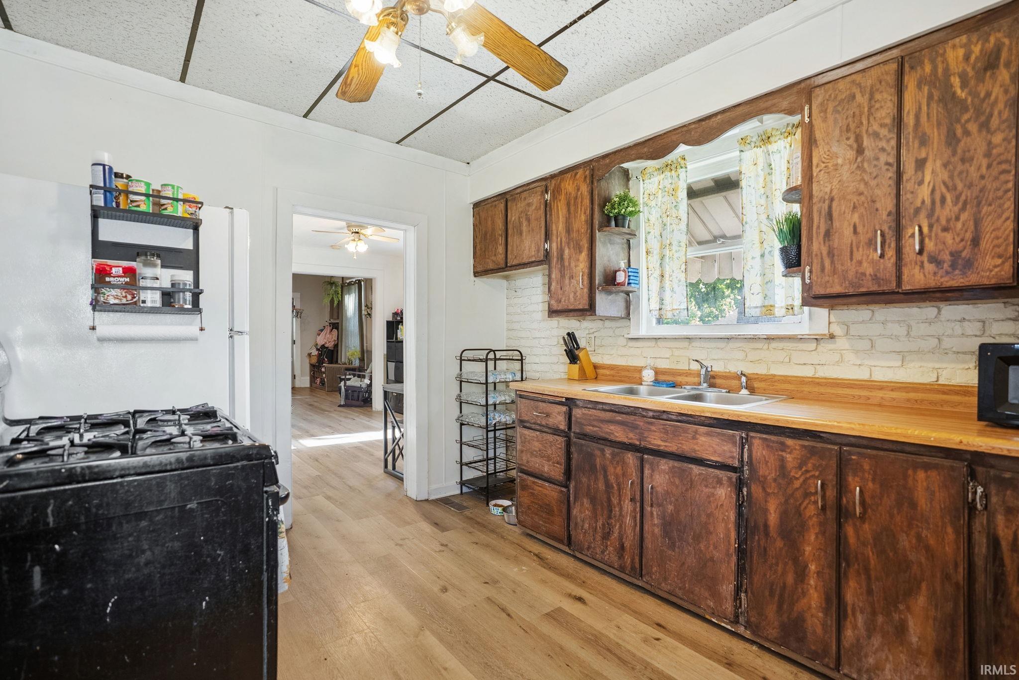 Kitchen featuring wood-finish flooring, wood cabinetry, light-toned countertops, a dual-basin sink, and a white brick-style backsplash