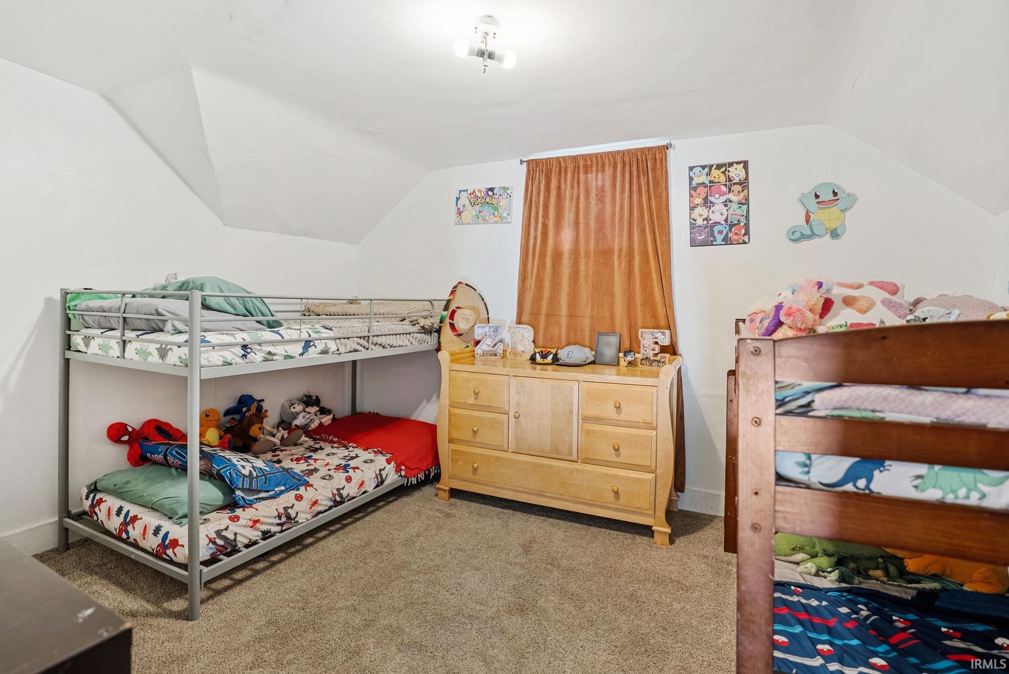 Carpeted room with a pitched ceiling and a window featuring brown drapes
