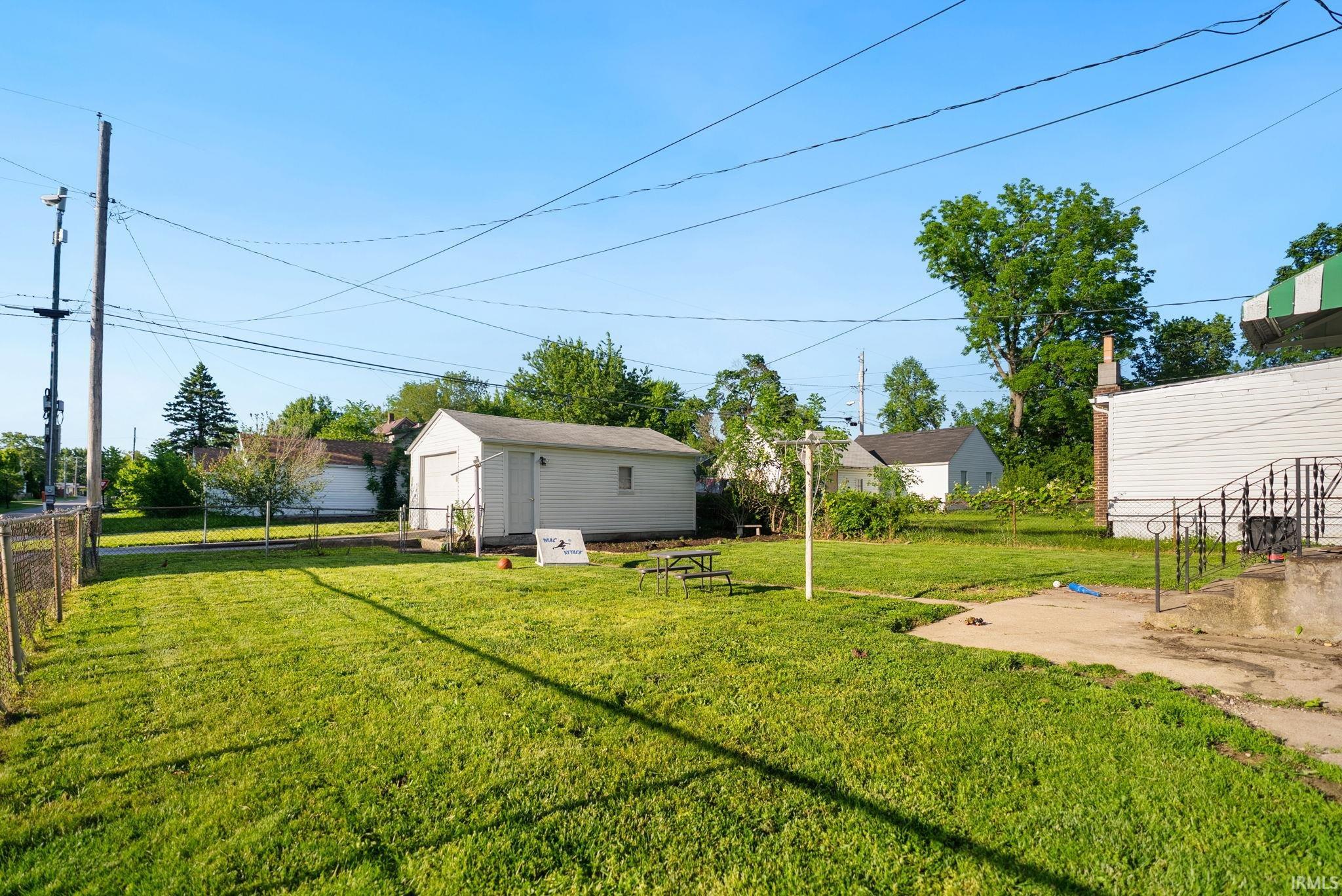 Expansive green lawn featuring a detached garage with a roll-up door, a clothesline pole, and a chain-link fence