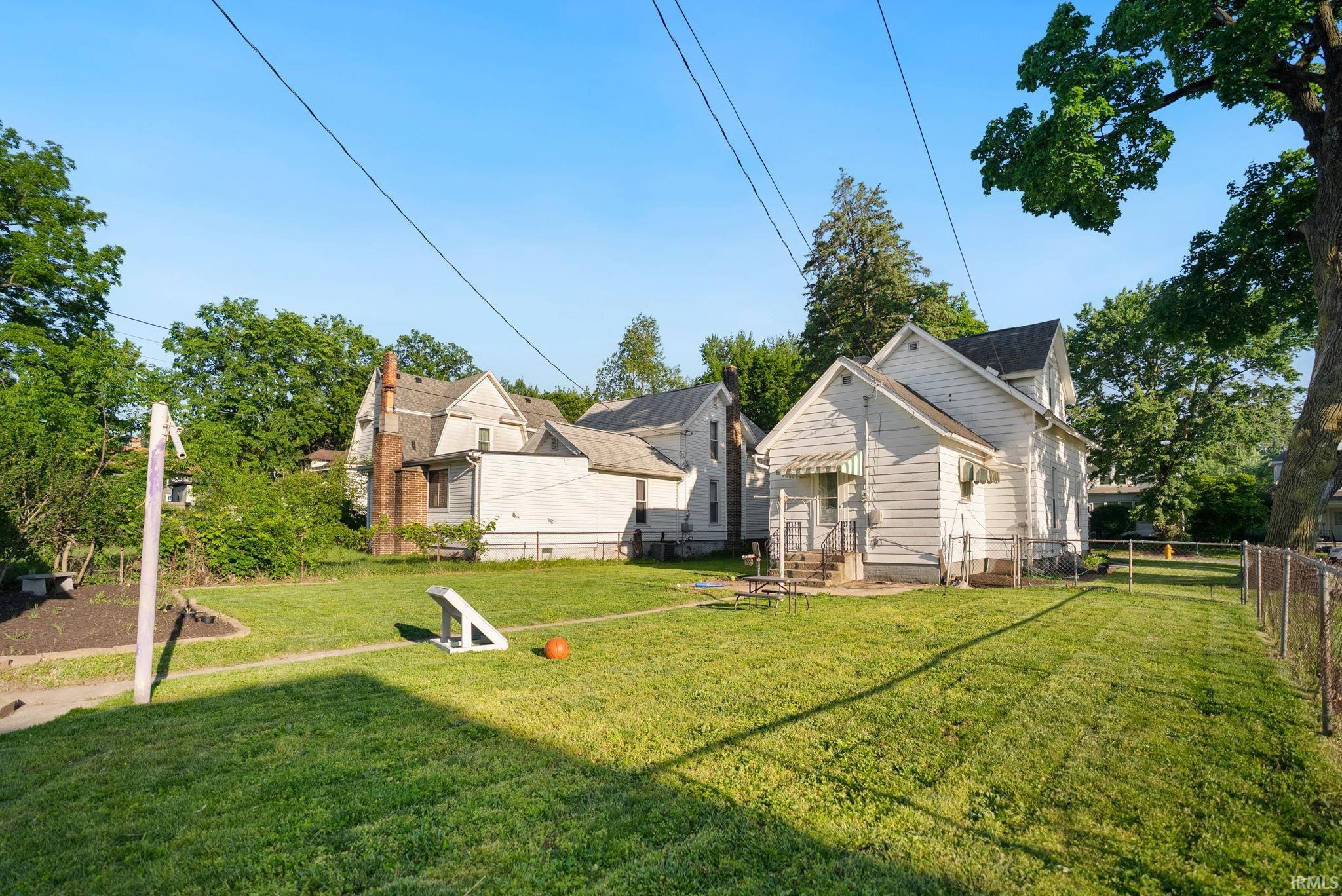 Spacious backyard with a lawn, partial chain-link fencing, and mature trees