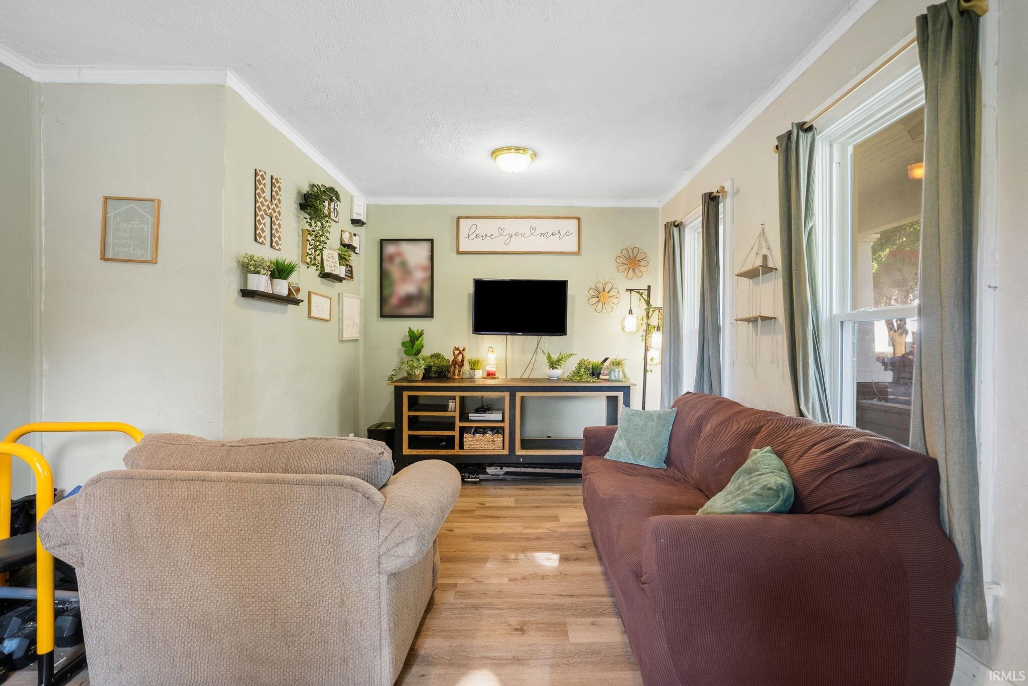 Living area with wood-finish flooring, light green wall finishes, white crown molding, and multiple windows providing natural light
