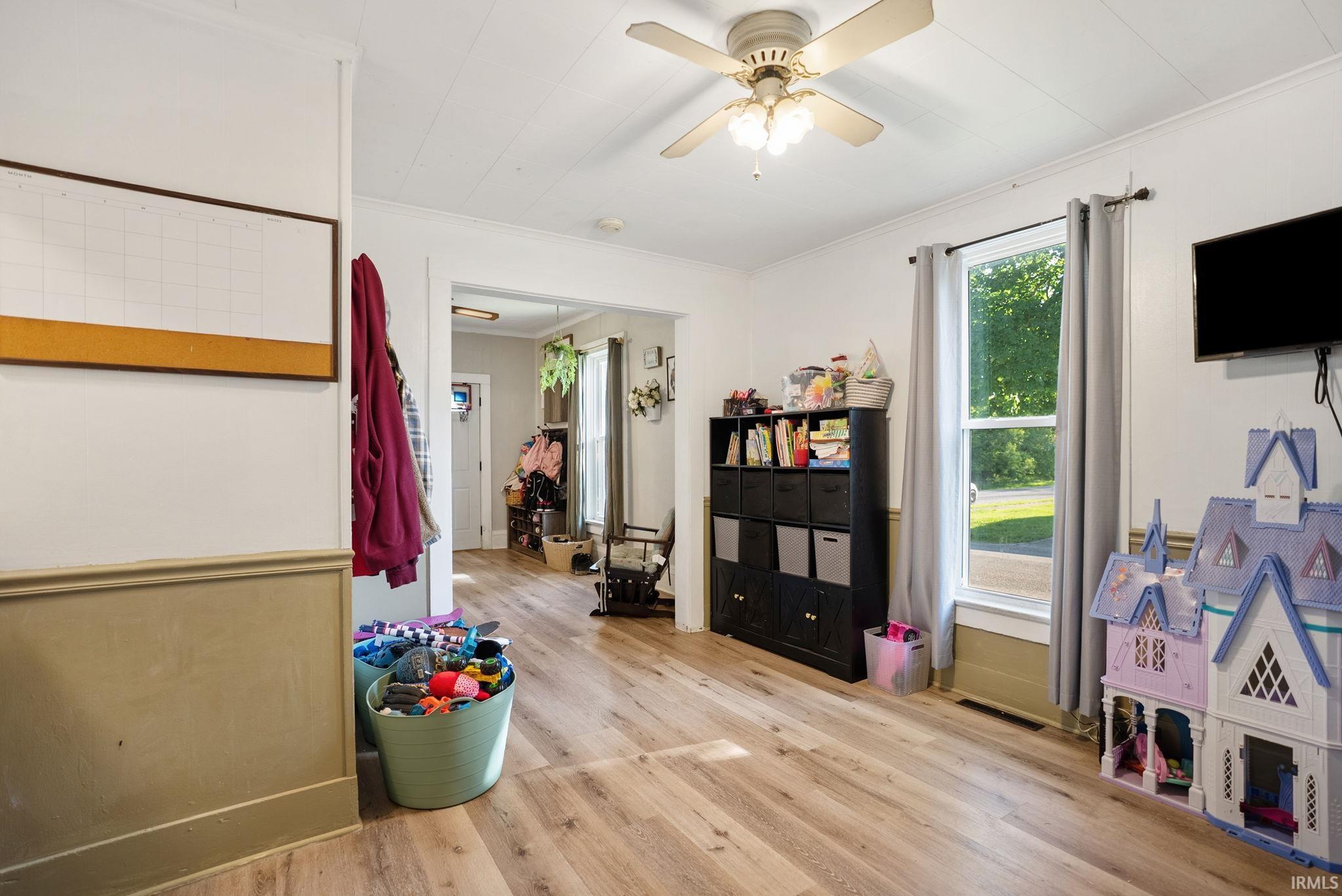 Hardwood-look flooring extends throughout this room, featuring light-colored walls and a ceiling fan with integrated lighting