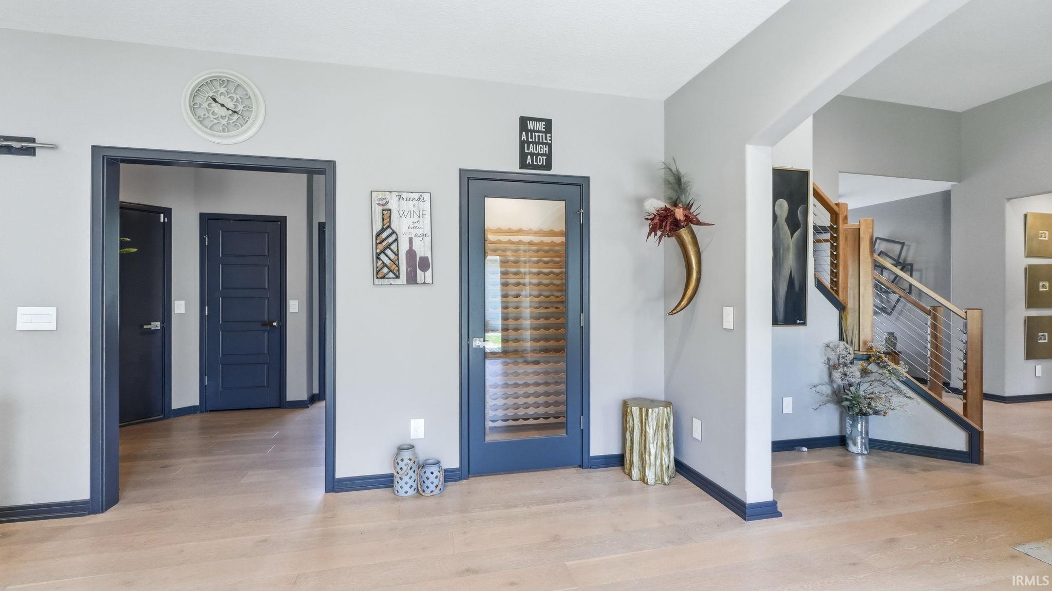 Entryway featuring wood-finish flooring, a built-in wine storage room with a glass-paneled door, a staircase with wood treads and a metal railing system, and dark trim details