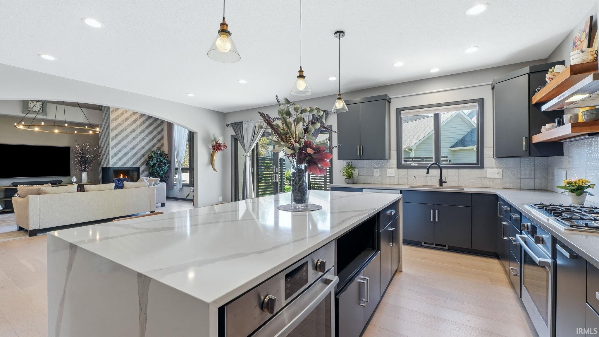 Contemporary kitchen featuring an oversized island with integrated appliances, light wood-finish flooring, dark cabinetry, and pendant lighting