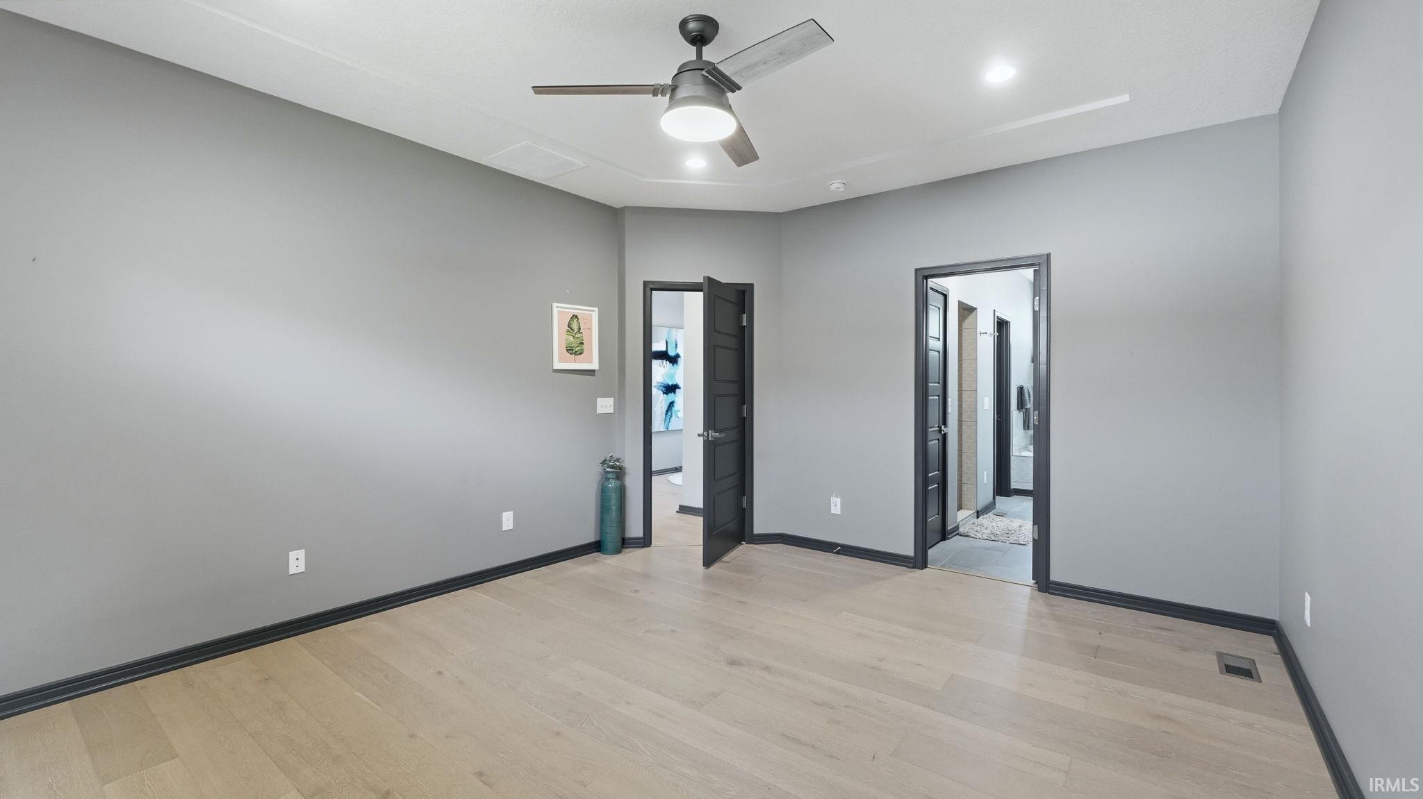 Spacious room featuring light wood-finish flooring, dark trim, and a ceiling fan with integrated lighting