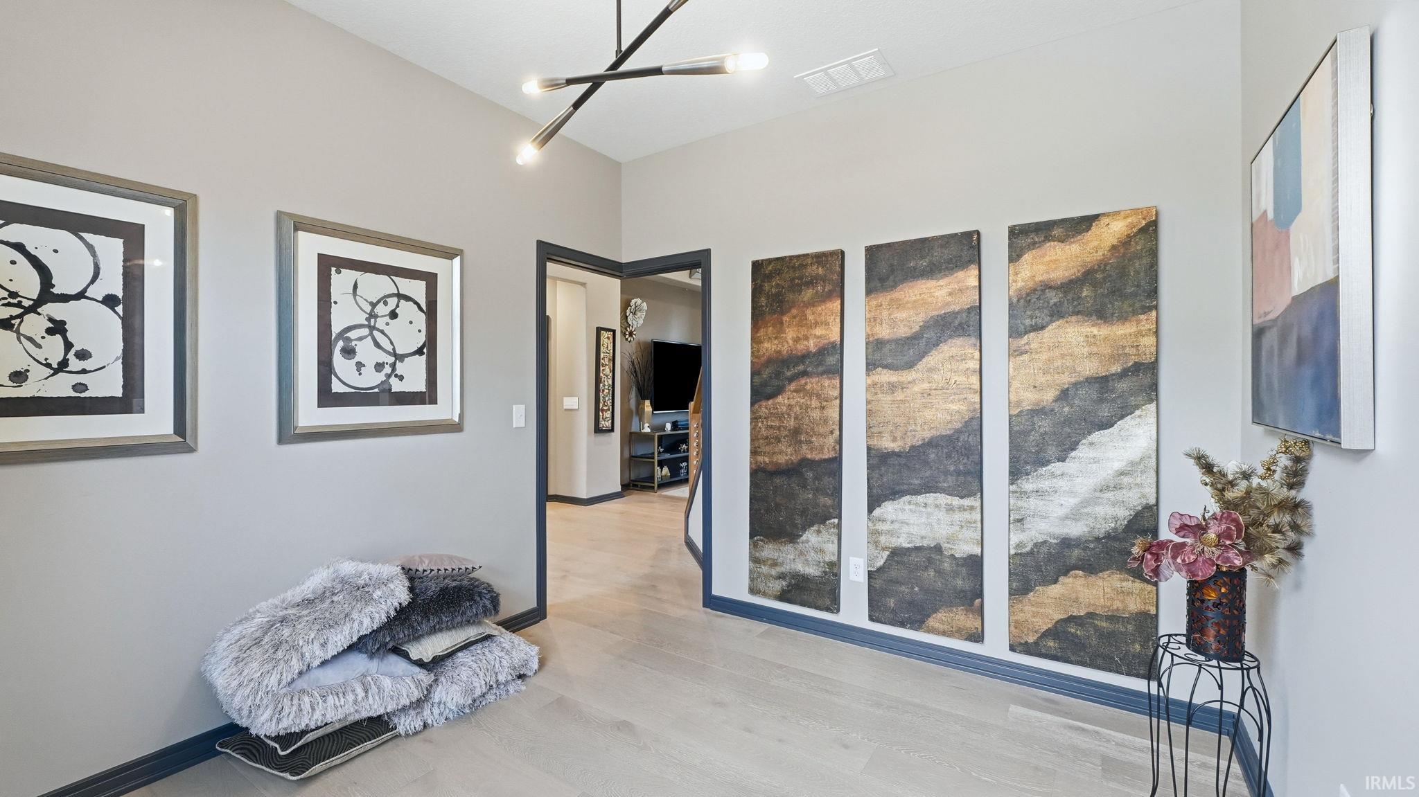 Hallway featuring light wood-finish flooring, vaulted ceilings, a linear chandelier, and dark trim