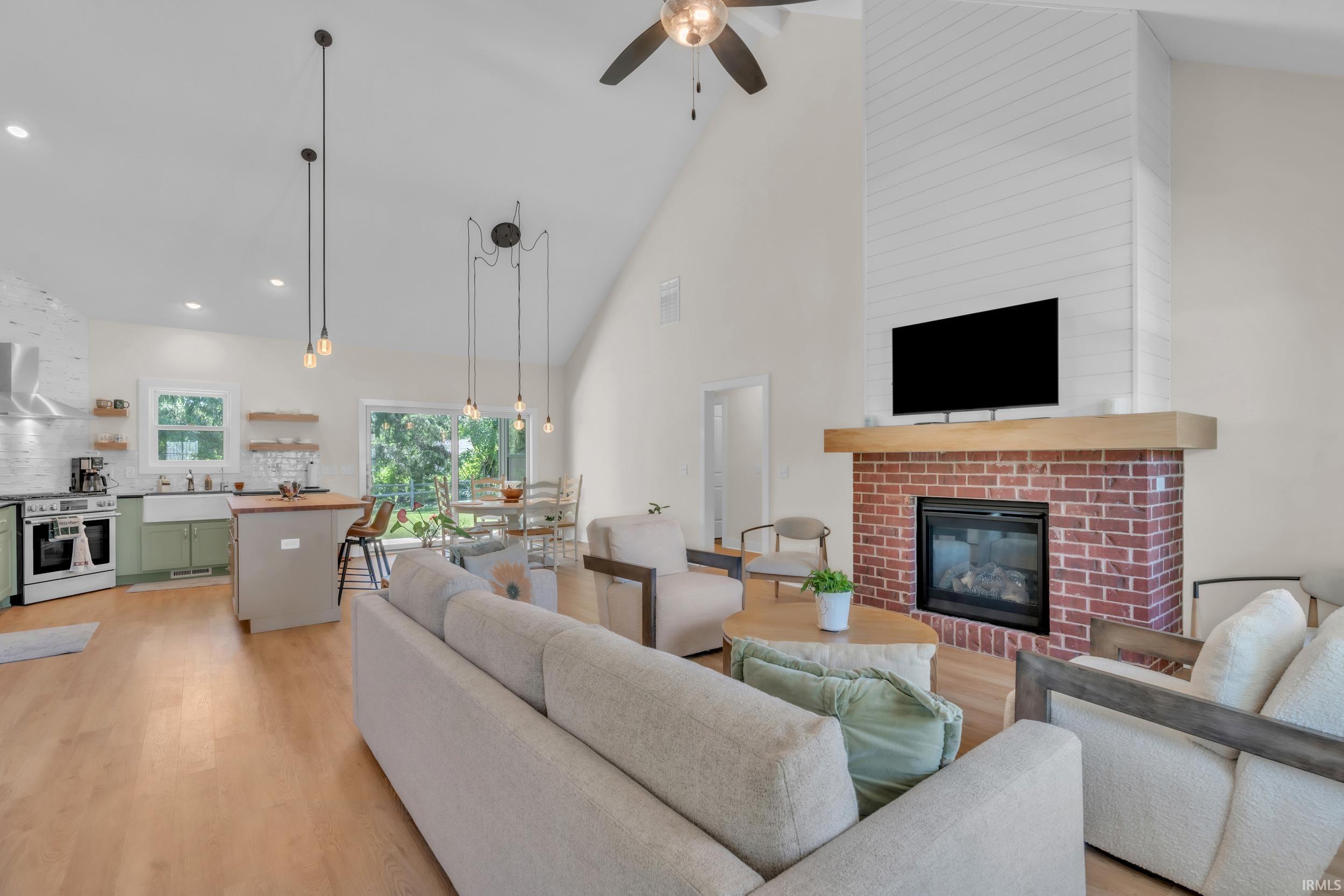 Vaulted living area with wood-finish flooring, a brick fireplace with shiplap surround and wood mantel, and integrated recessed lighting