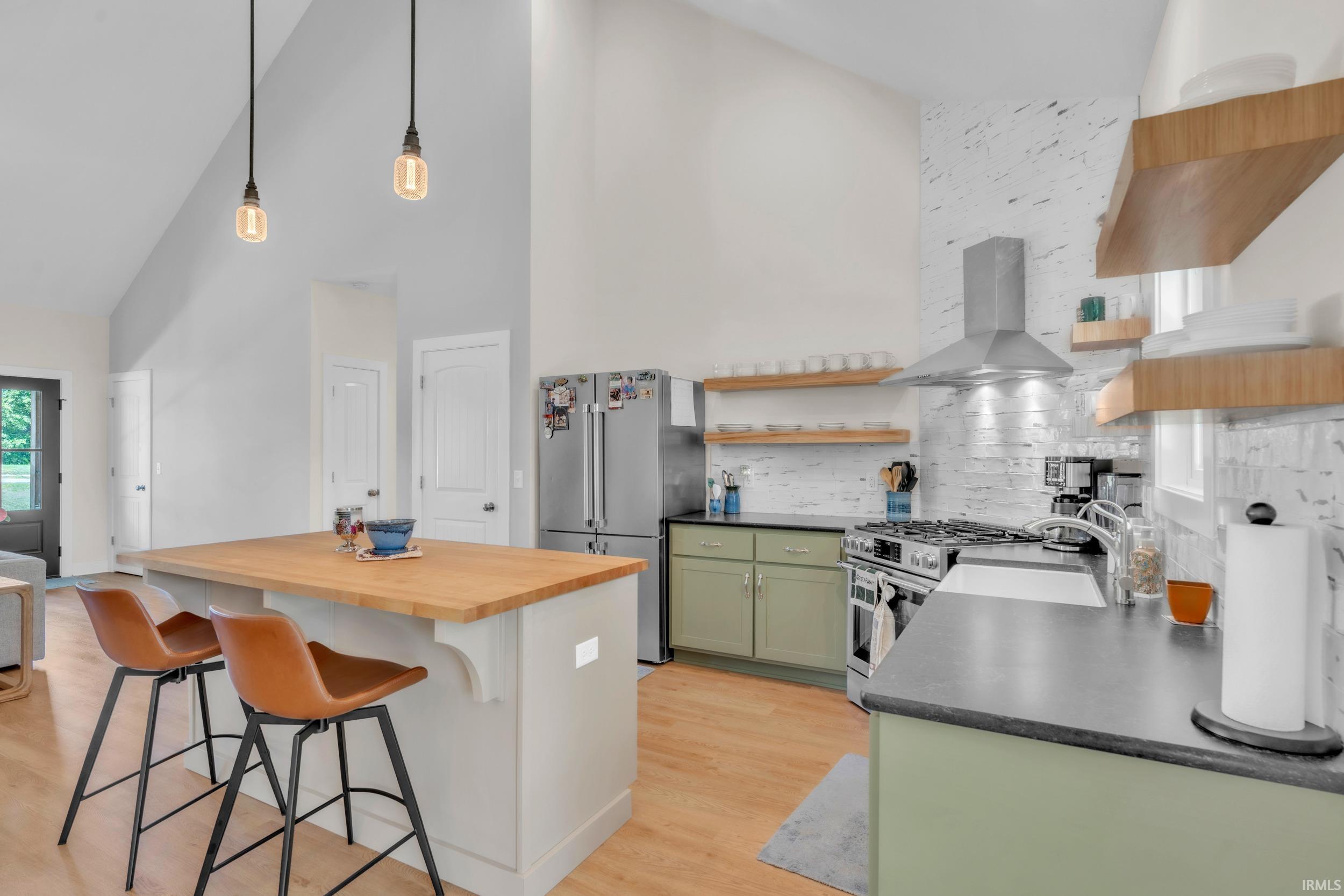 Kitchen featuring a central island with a wood-finish countertop, pendant lighting, stainless steel appliances, open wood-finish shelving, and a patterned tile backsplash