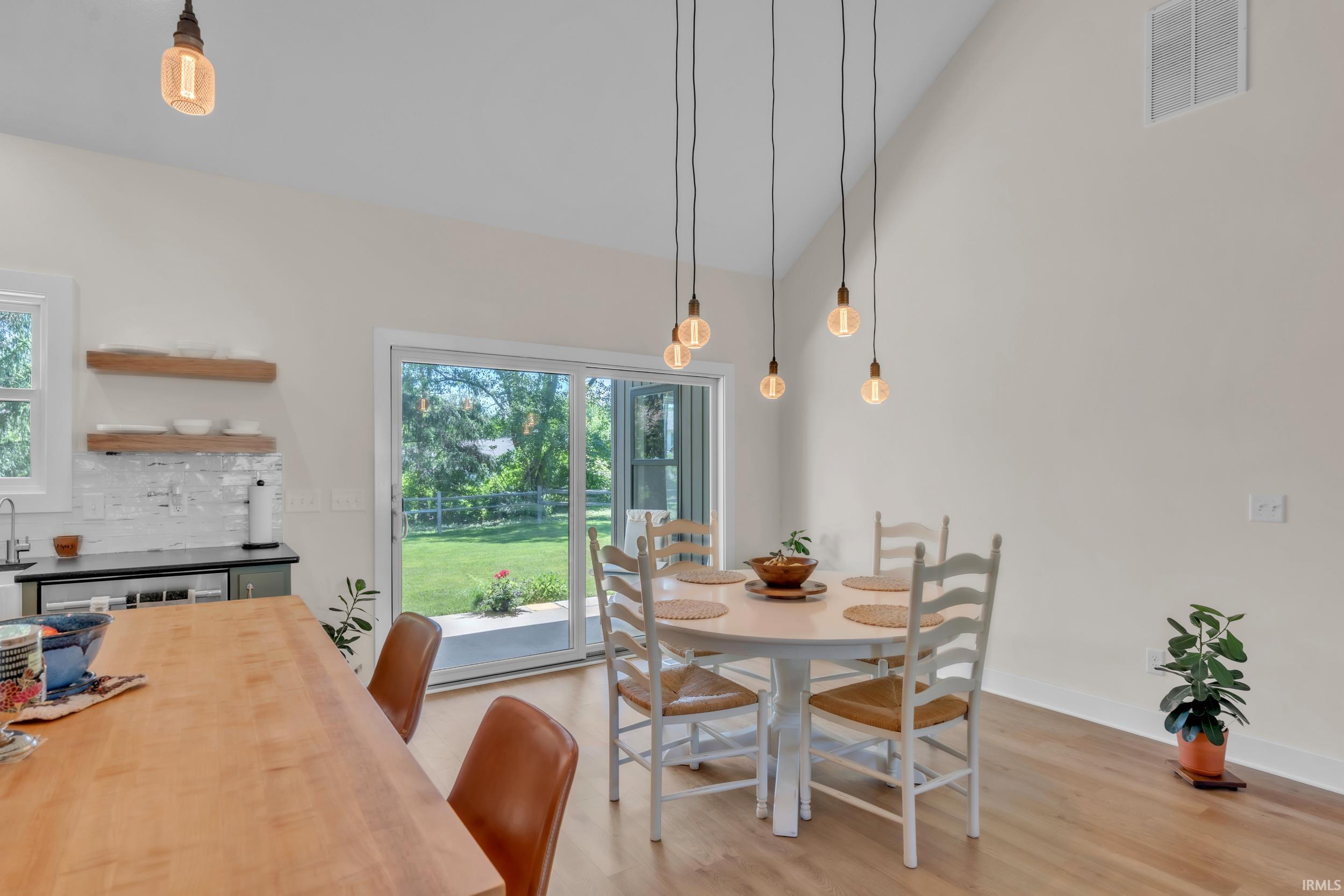 Vaulted ceiling dining area featuring contemporary pendant lighting, wood-finish flooring, and direct access to the outdoor space via a sliding glass door